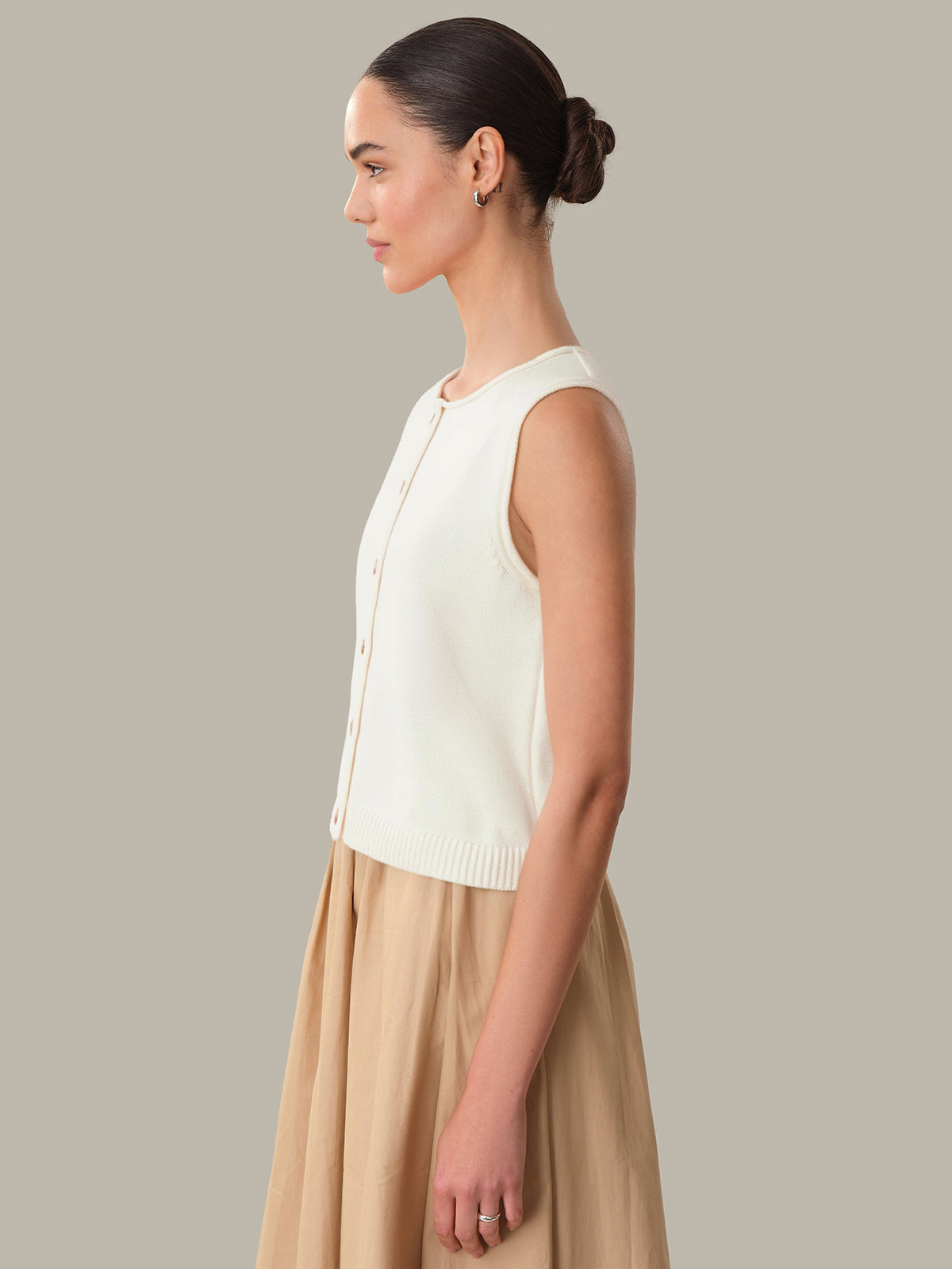 Woman wearing a white sleeveless top and beige skirt against a neutral background