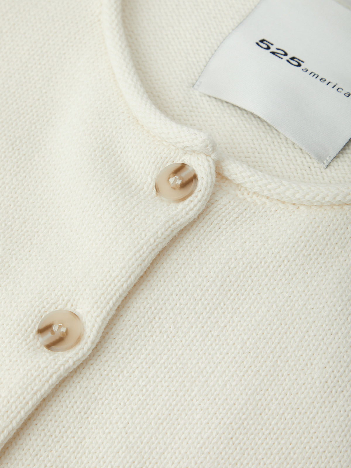 Close-up of a cream-colored garment with buttons and a tag displaying '525 America'.