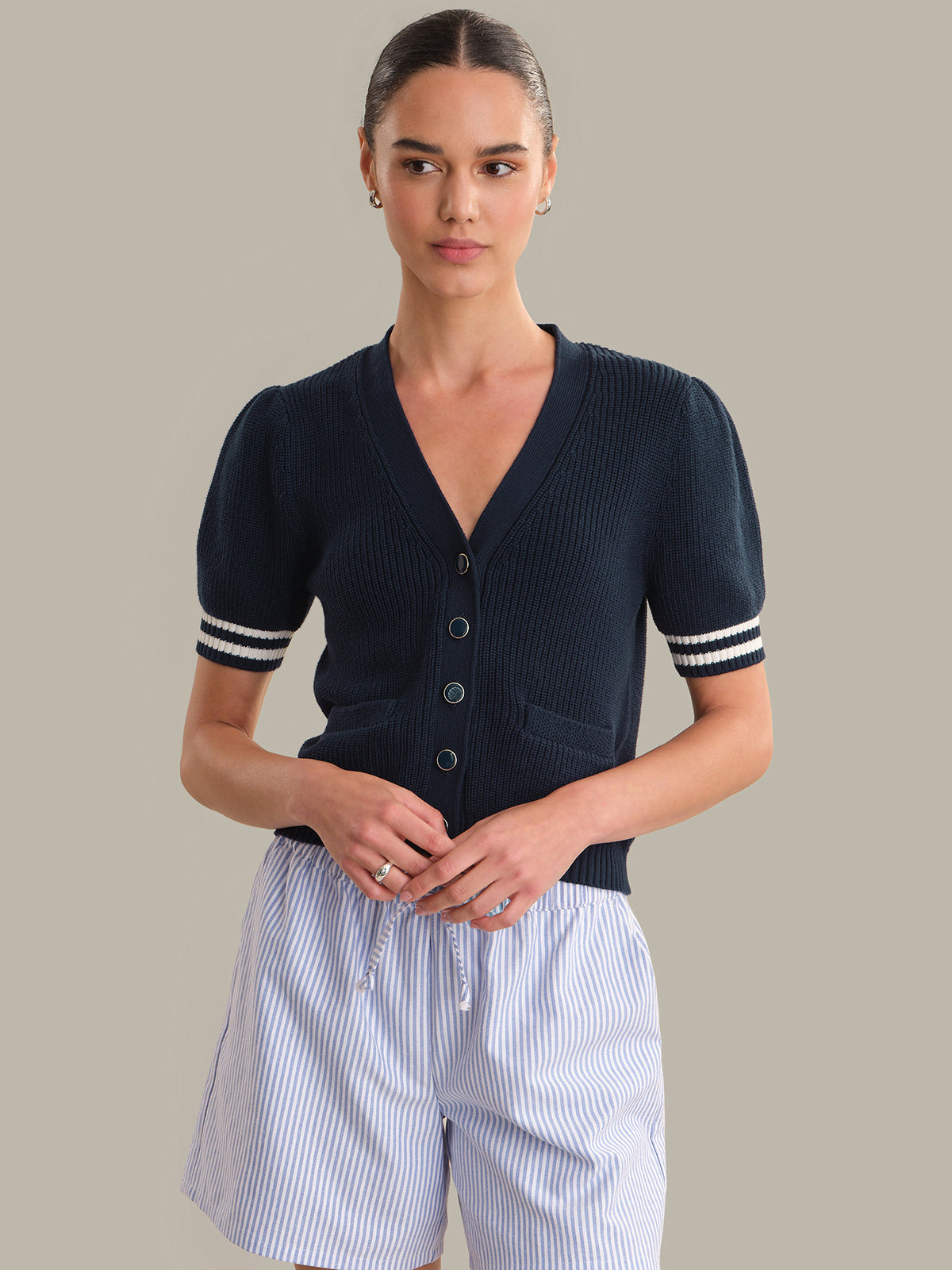 Woman wearing a navy blue cardigan with white trim on a gray background