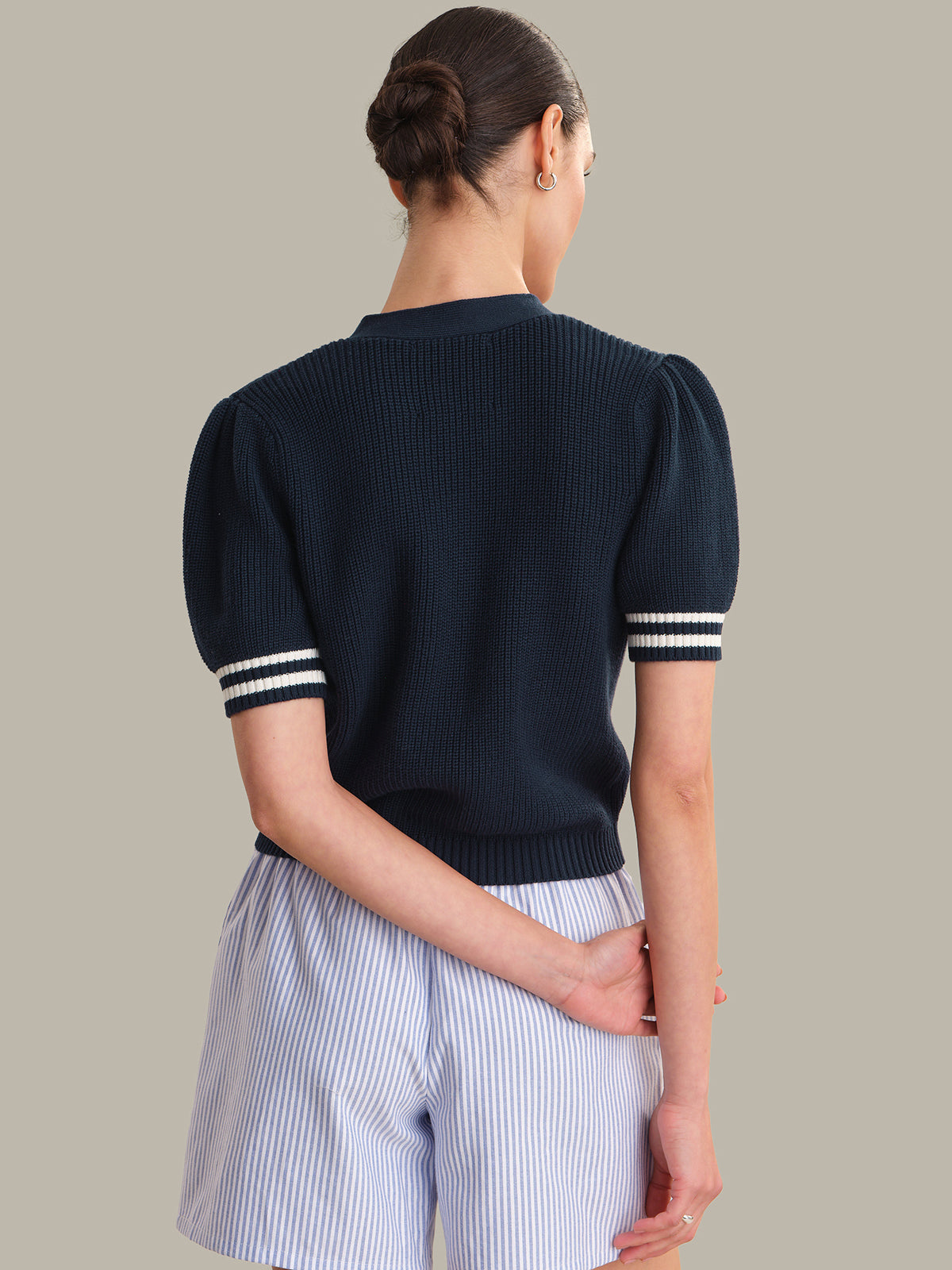 Woman wearing a navy sweater with white trim on a plain background