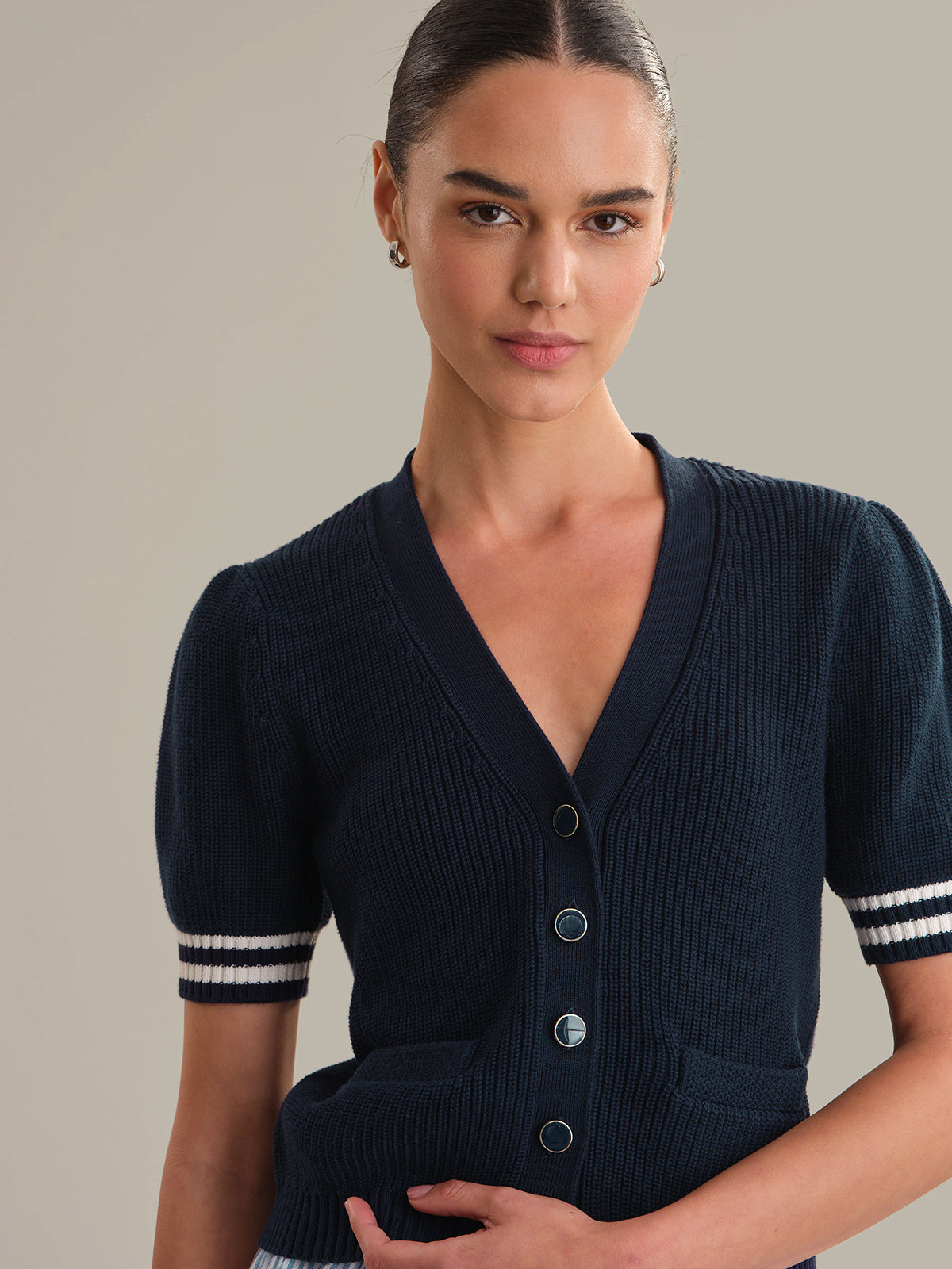 Woman wearing a navy blue cardigan with white trim on a neutral background