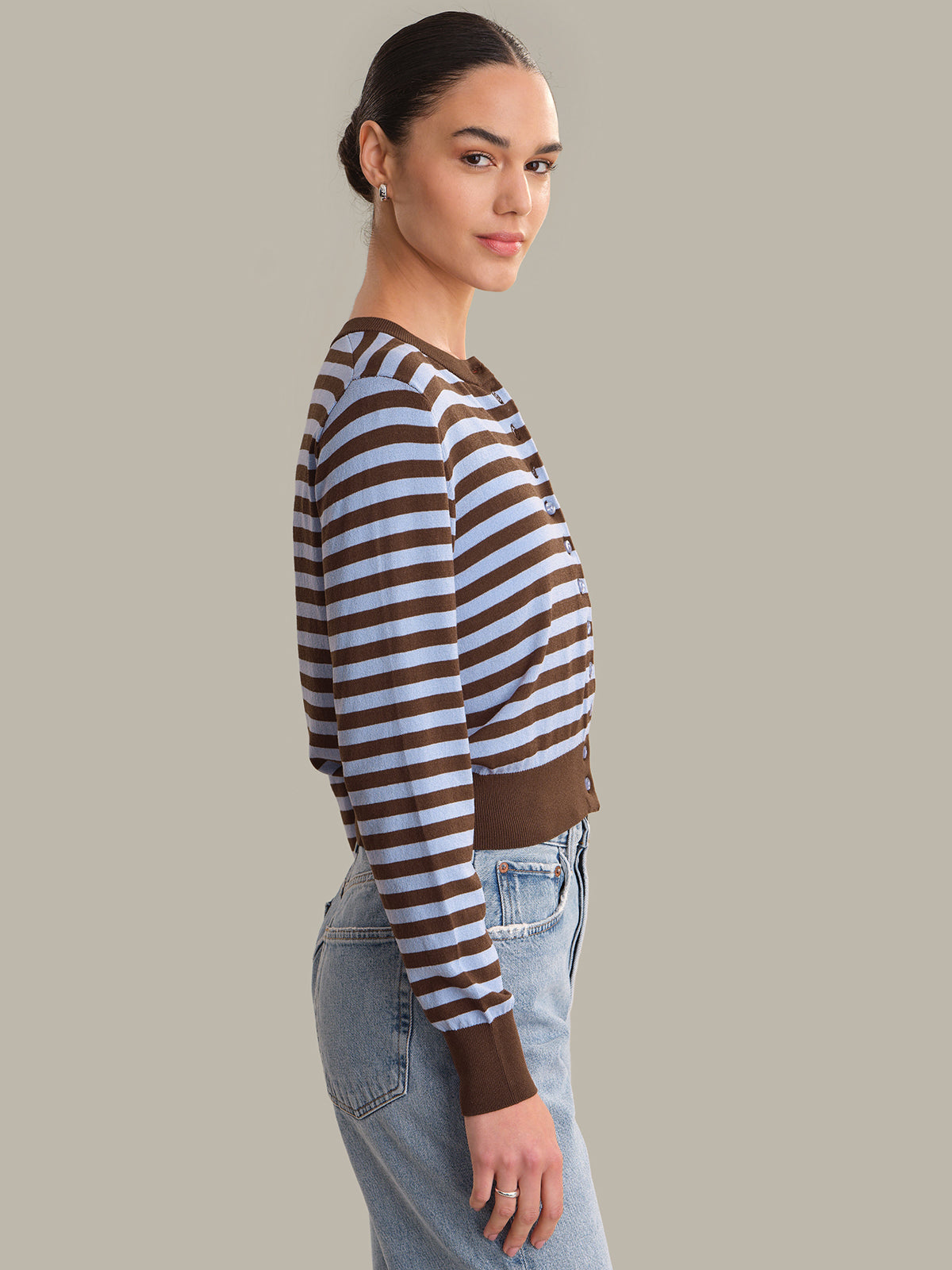 Woman wearing a brown and white striped cardigan with blue jeans on a plain background