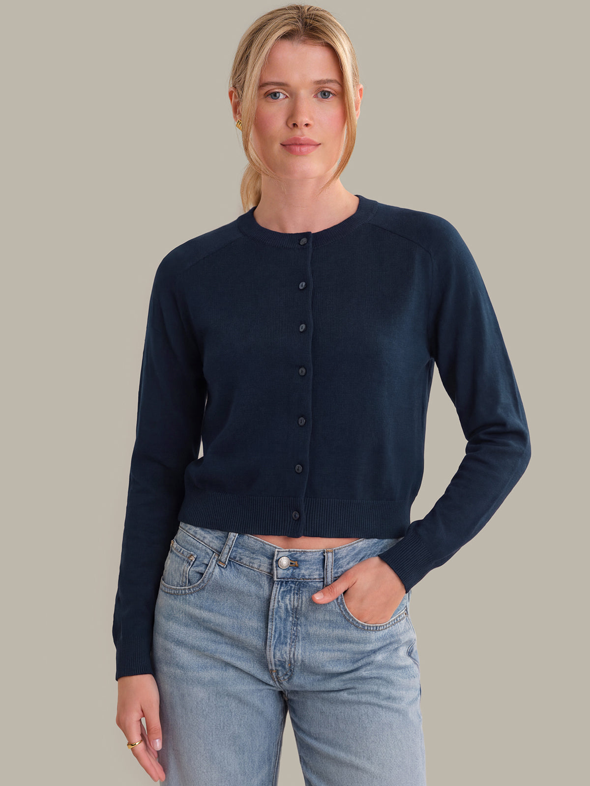 Woman wearing a navy cardigan and light blue jeans against a neutral background