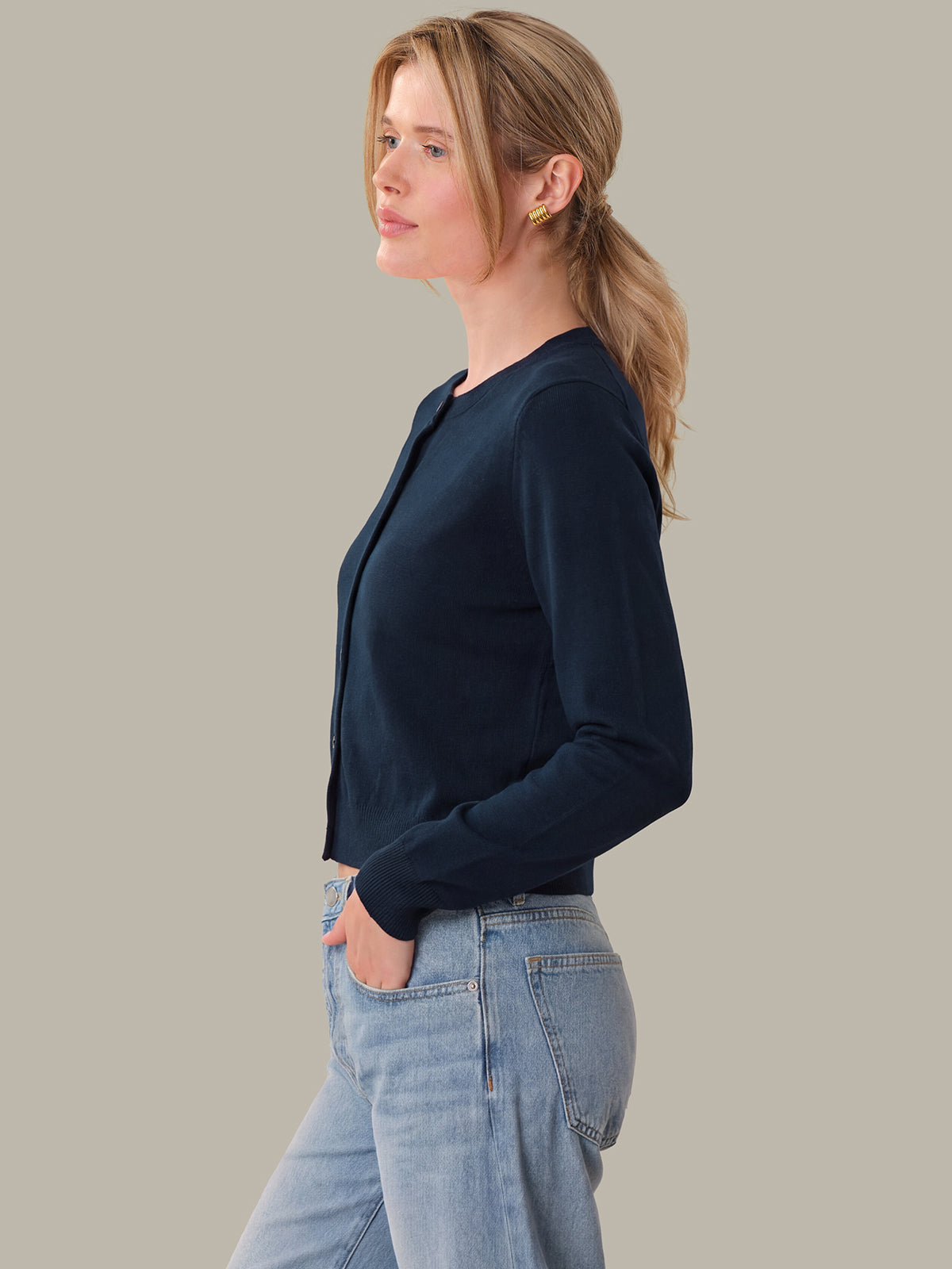 Woman wearing a navy blazer and light blue jeans against a neutral background