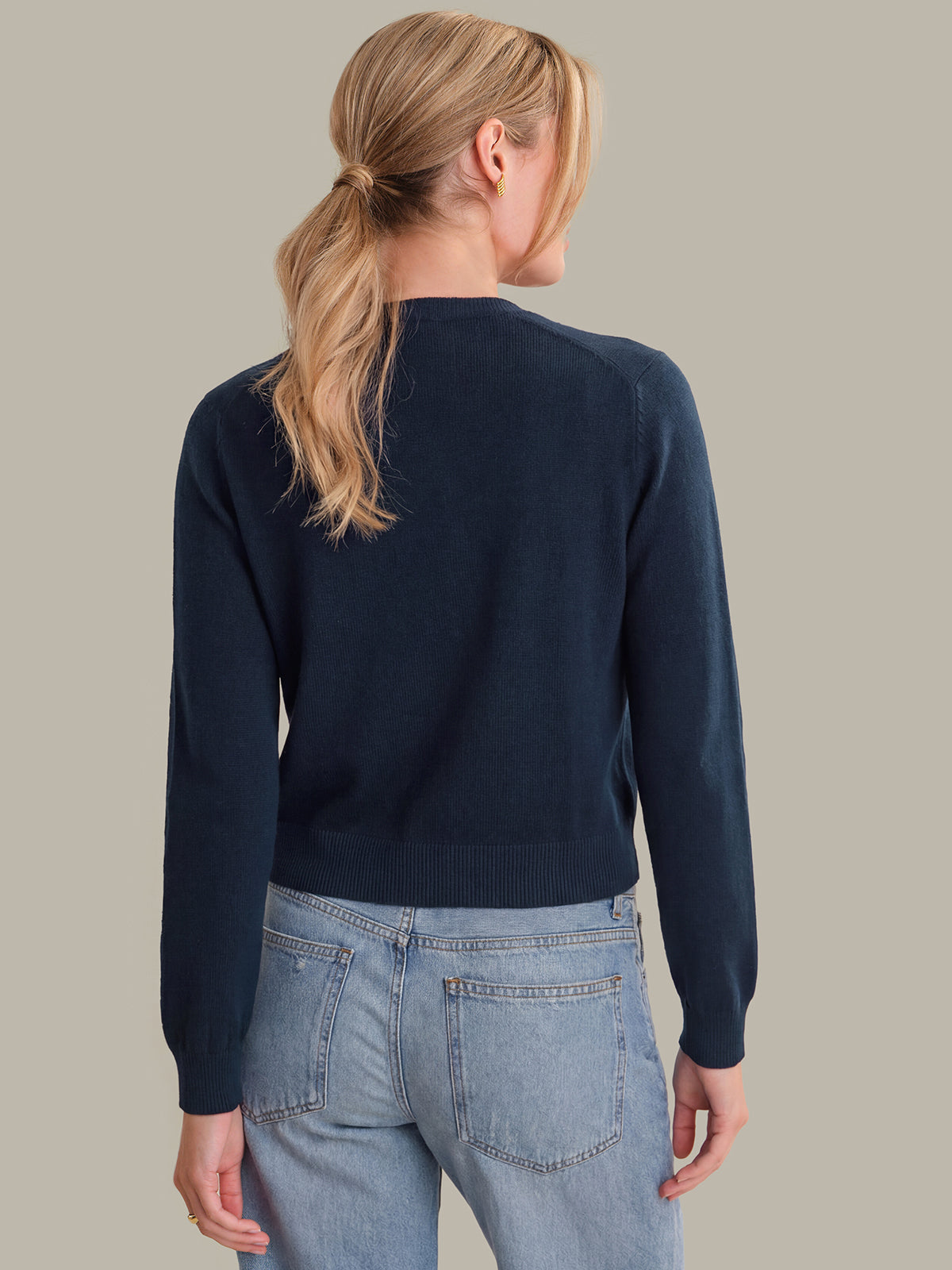 Person wearing a navy sweater and light blue jeans on a neutral background