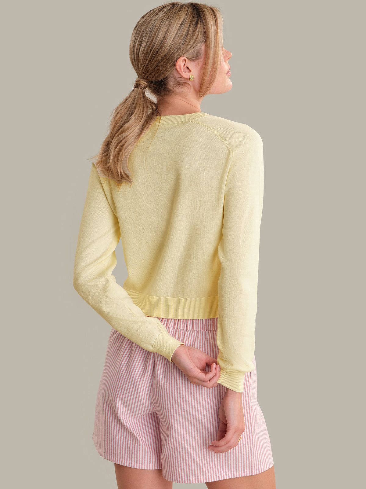 Woman wearing a light yellow sweater and pink shorts on a neutral background