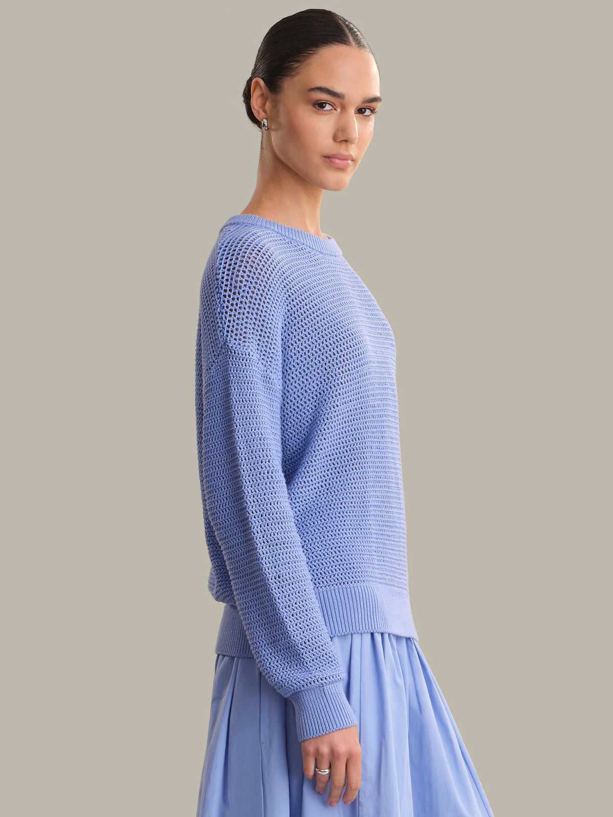 Woman wearing a light blue knitted sweater and skirt against a neutral background