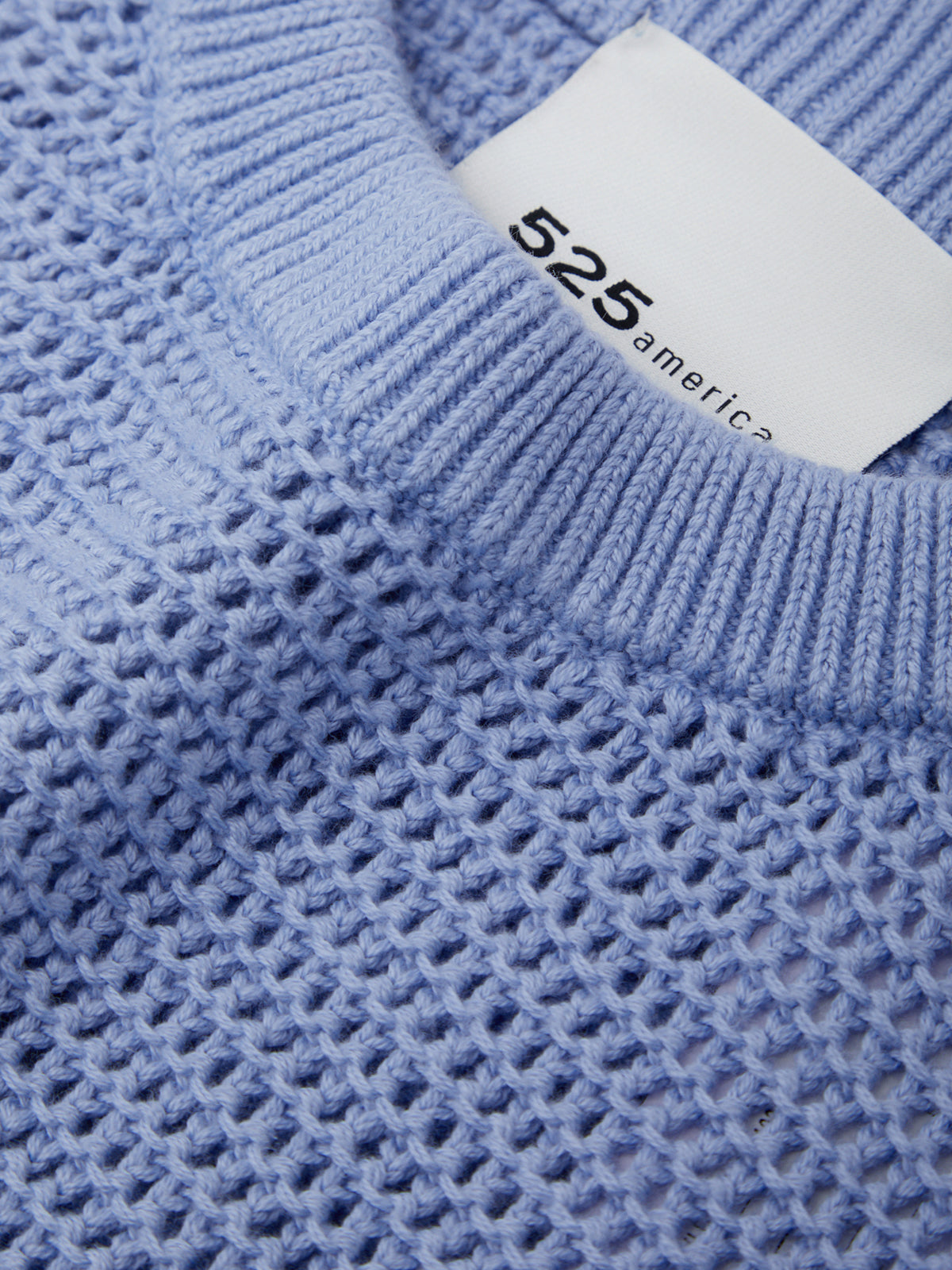 Close-up of a blue textured sweater with a white label displaying '525 America'.