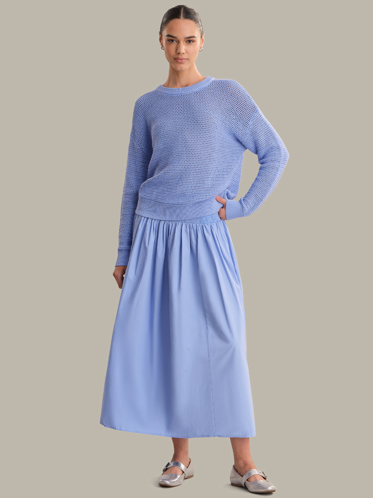 Woman wearing a light blue sweater and skirt set on a plain background