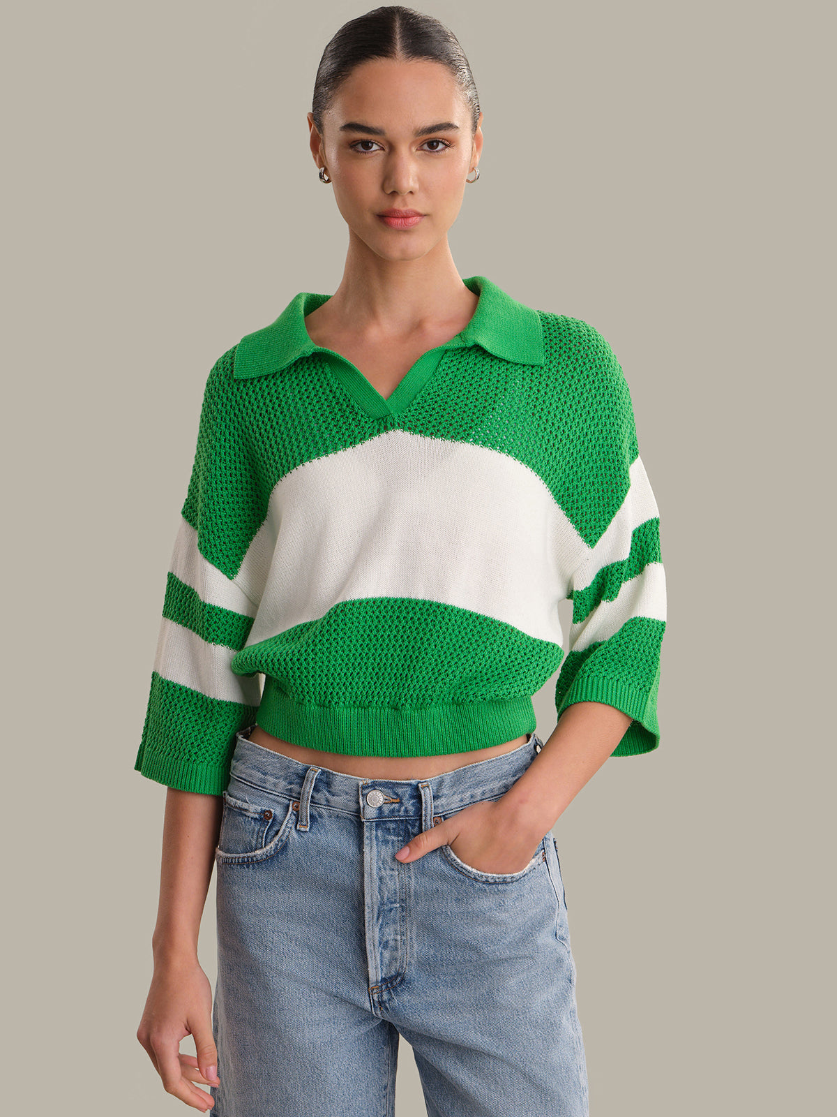 Woman wearing a green and white striped sweater with blue jeans on a neutral background