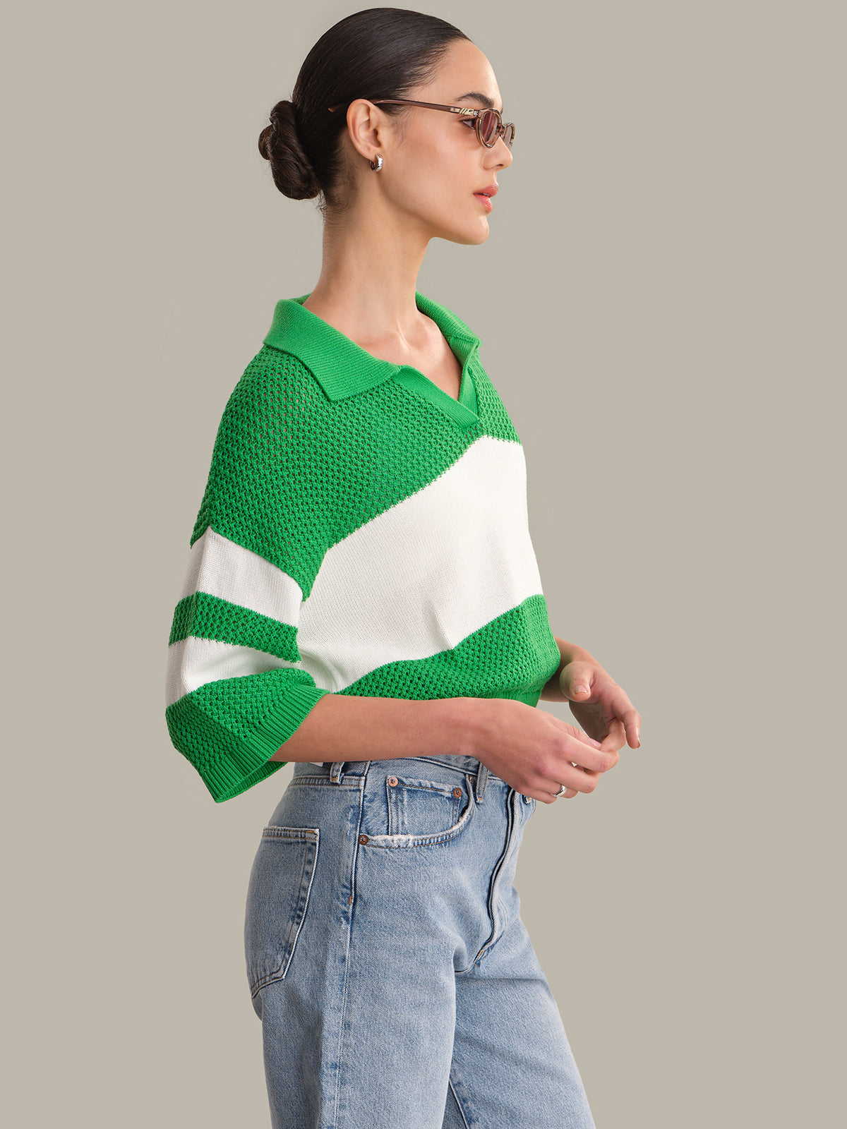 Woman wearing a green and white striped sweater with blue jeans on a gray background