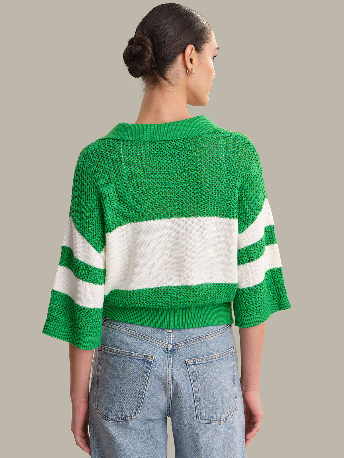 Person wearing a green and white striped sweater with blue jeans on a neutral background