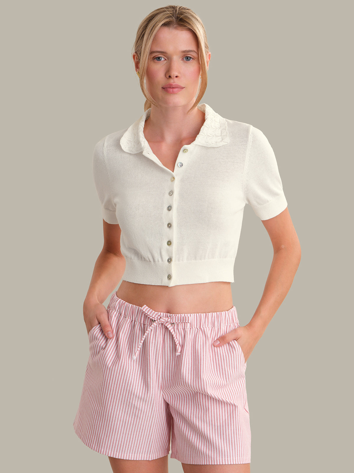 Woman wearing a white cropped top and pink striped shorts on a gray background