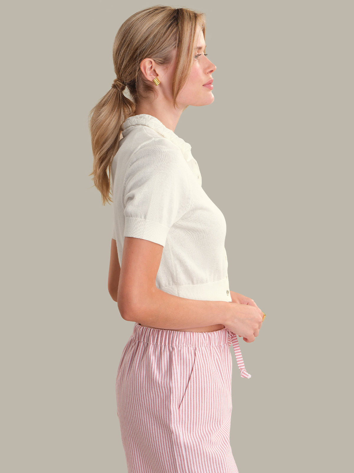 Woman wearing a white shirt and pink striped pants against a gray background