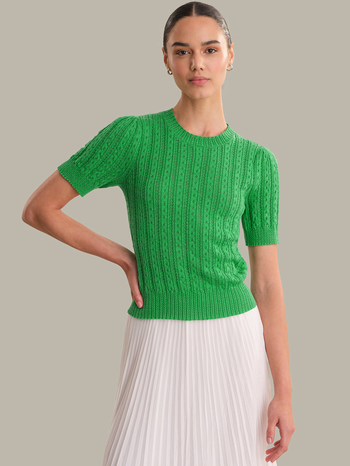 Woman wearing a green knitted top and white pleated skirt on a gray background