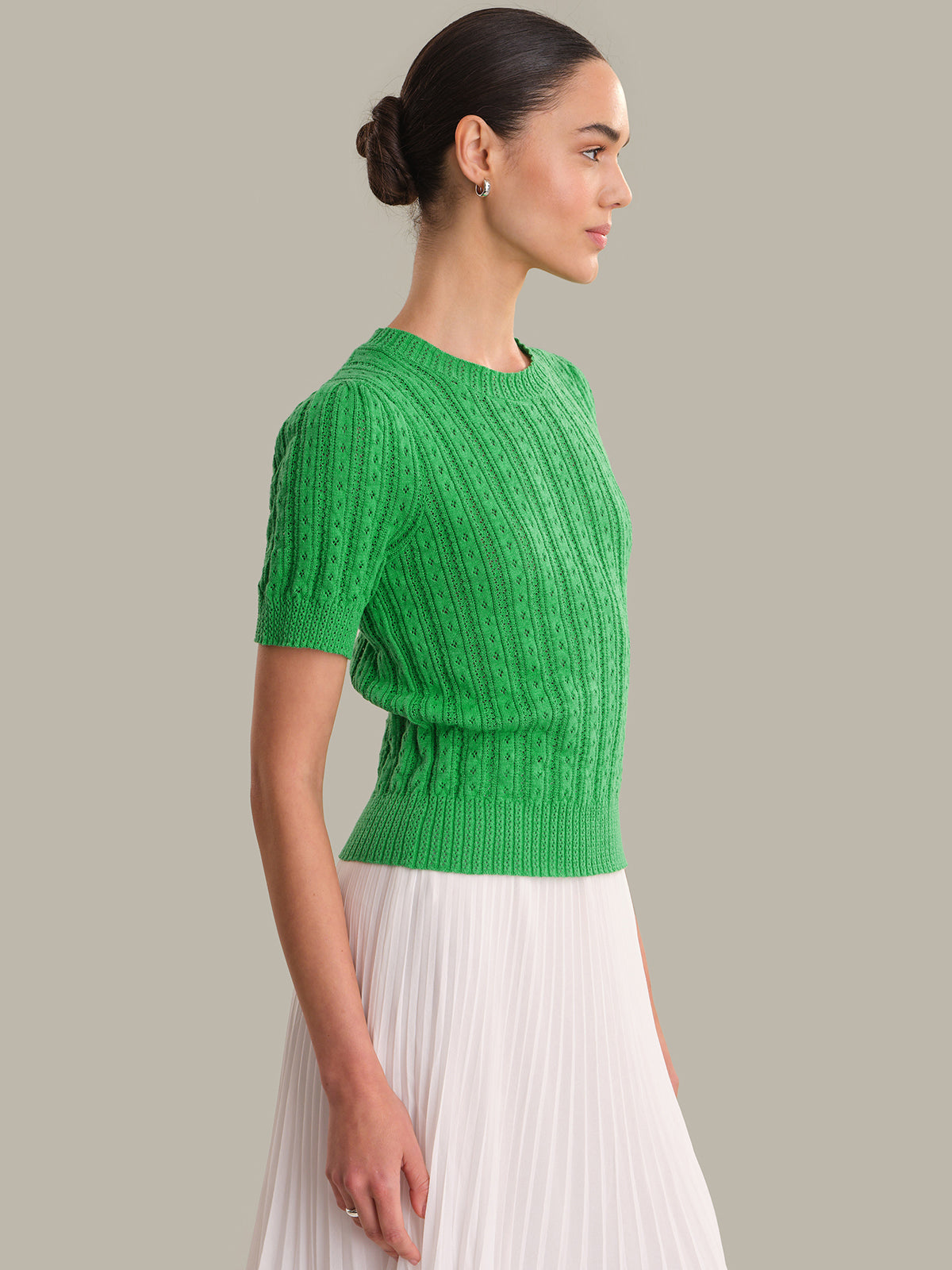 Woman wearing a green knitted top and white pleated skirt on a gray background