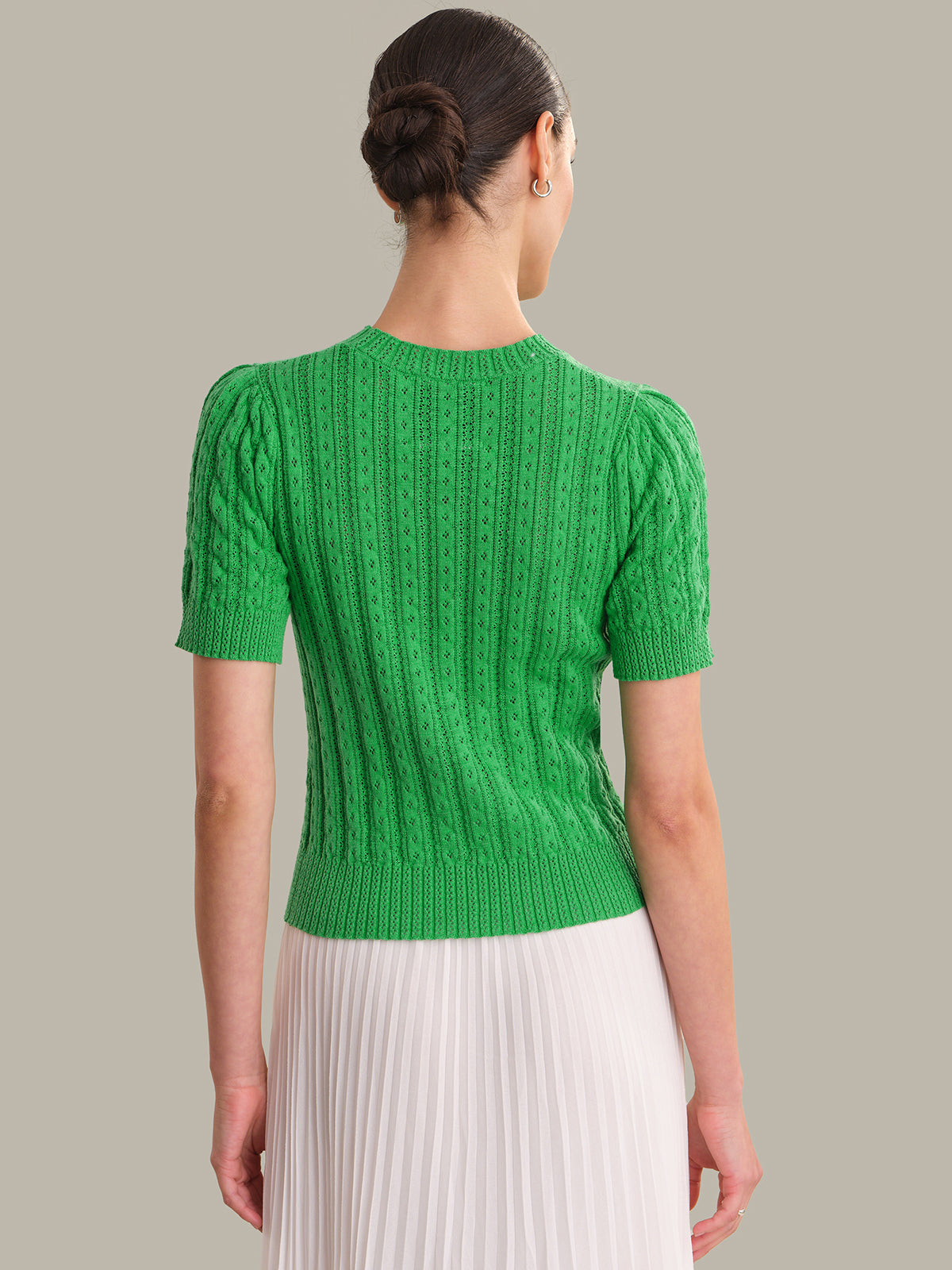 Person wearing a green knitted top with a plain background