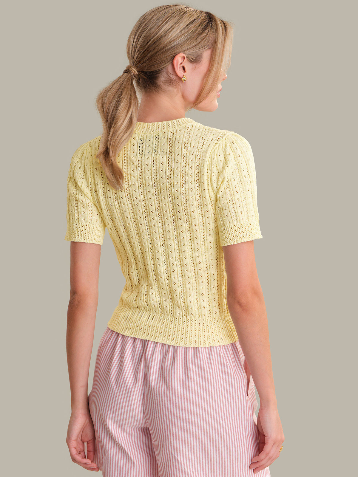 Woman wearing a yellow knitted top and pink pants against a neutral background