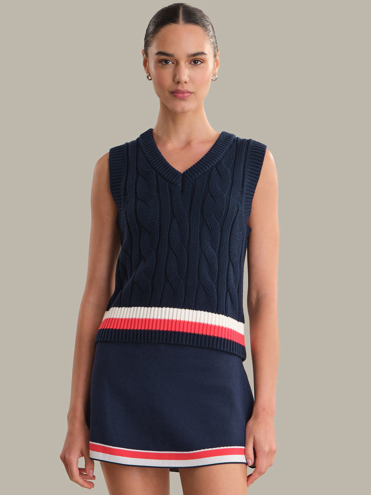 Woman wearing a navy sleeveless sweater with a red and white stripe on a neutral background