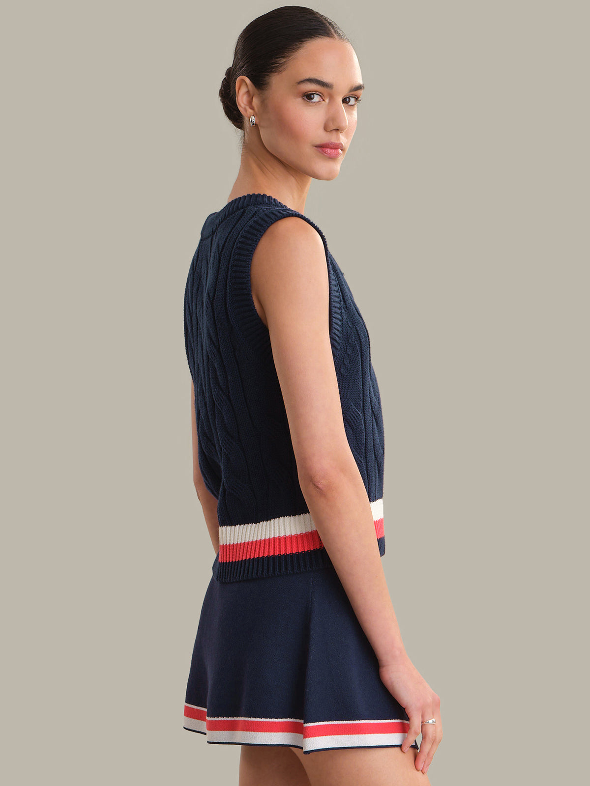 Woman wearing a navy sleeveless vest with red and white trim on a gray background