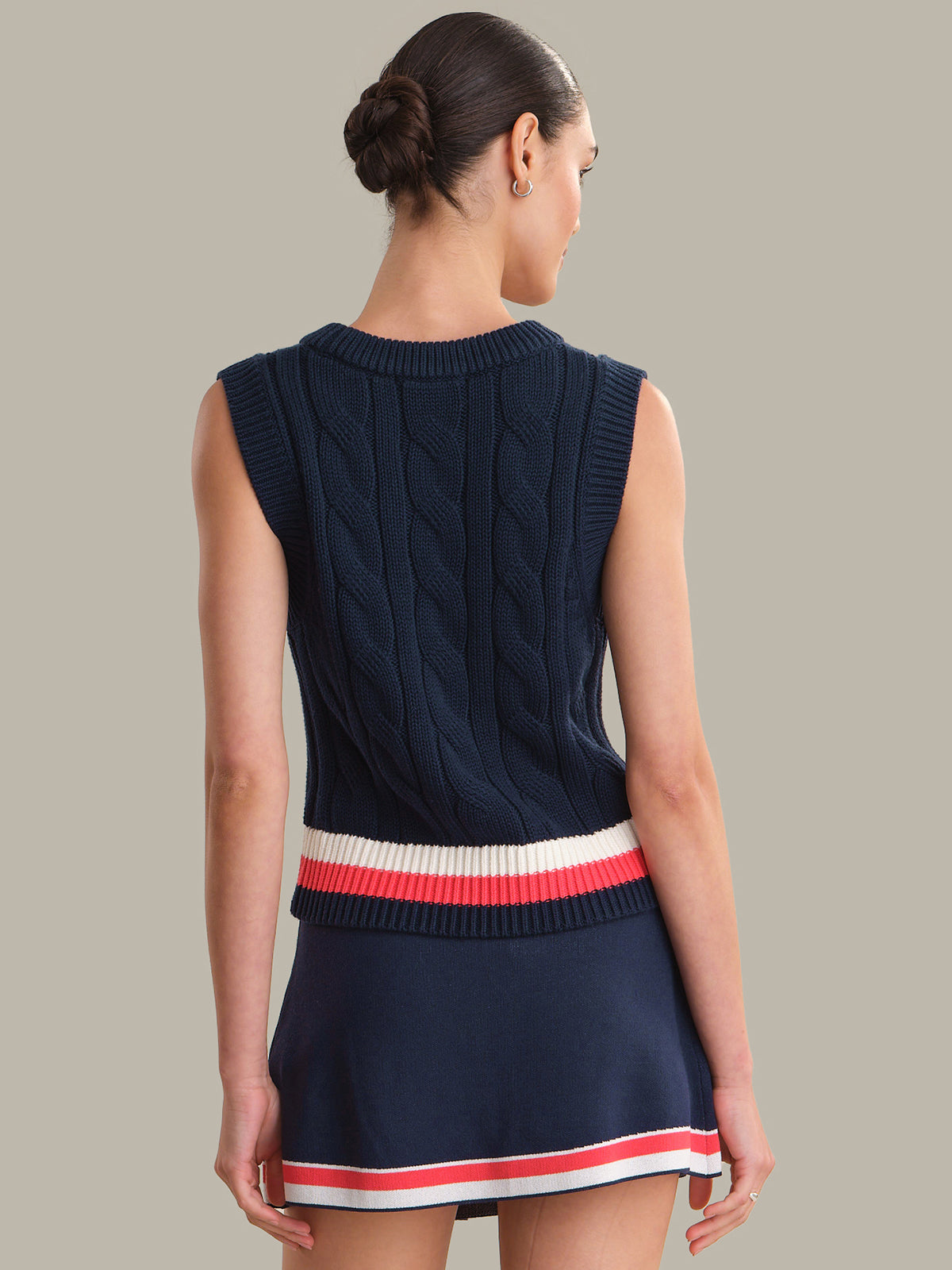 Woman wearing a navy blue sleeveless knitted top with a red and white striped hem on a neutral background