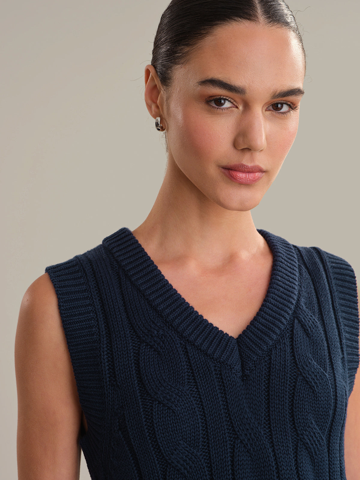 Woman wearing a navy blue sleeveless knitted top against a neutral background
