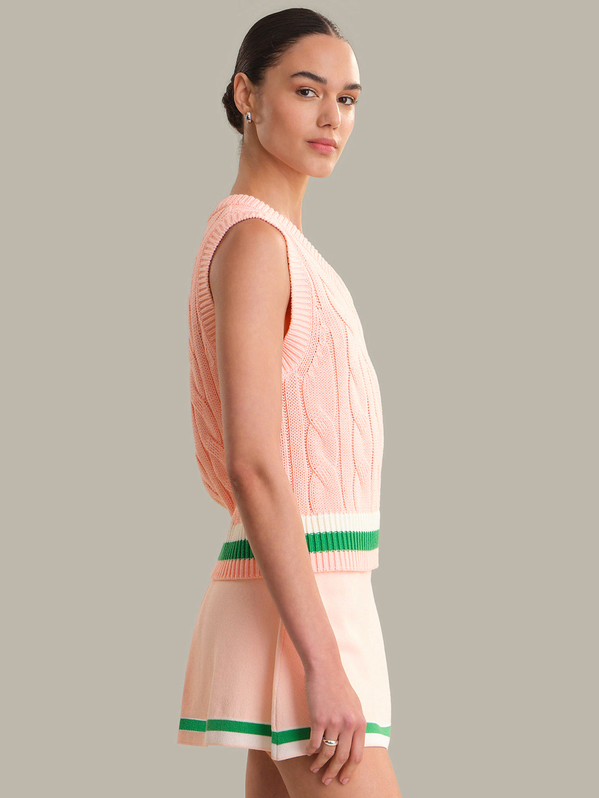 Woman wearing a pink sleeveless dress with green trim on a gray background