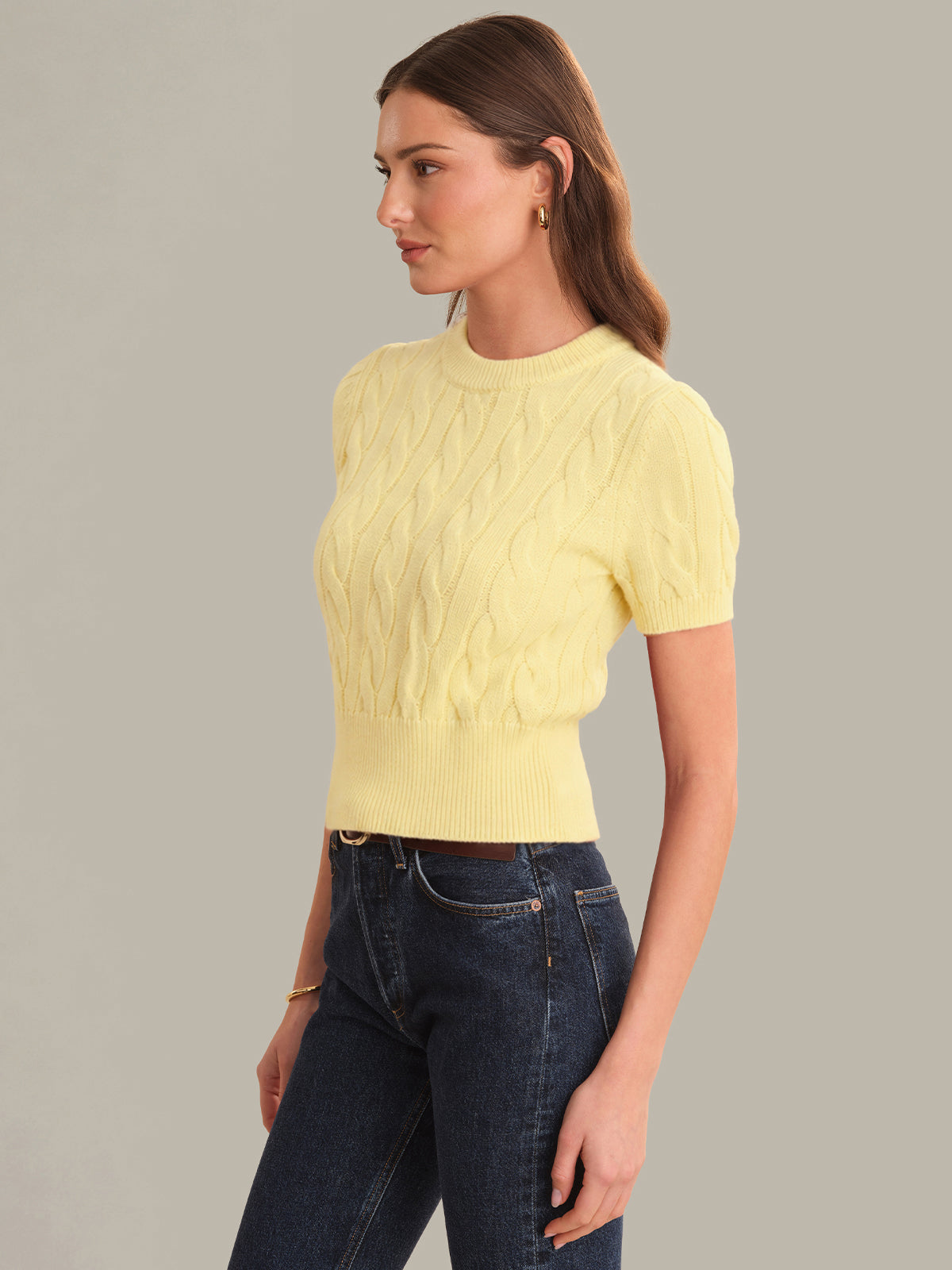 Woman wearing a yellow cable knit sweater and blue jeans on a gray background