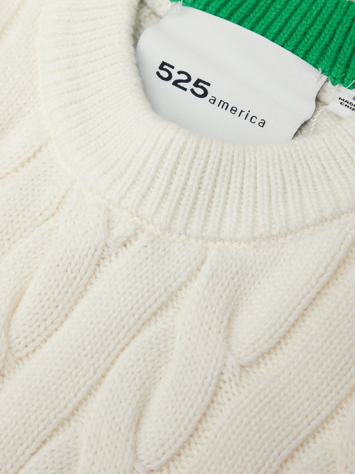 Close-up of a cable-knit sweater with a brand label on a white background