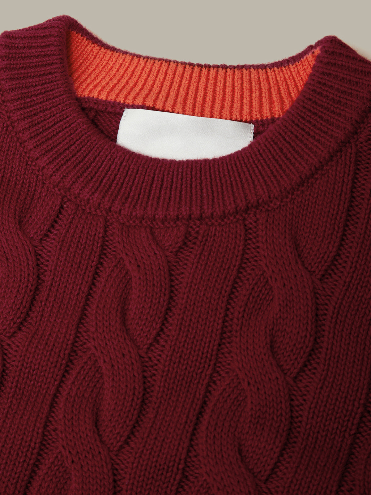 Close-up of a maroon cable knit sweater with an orange lining.