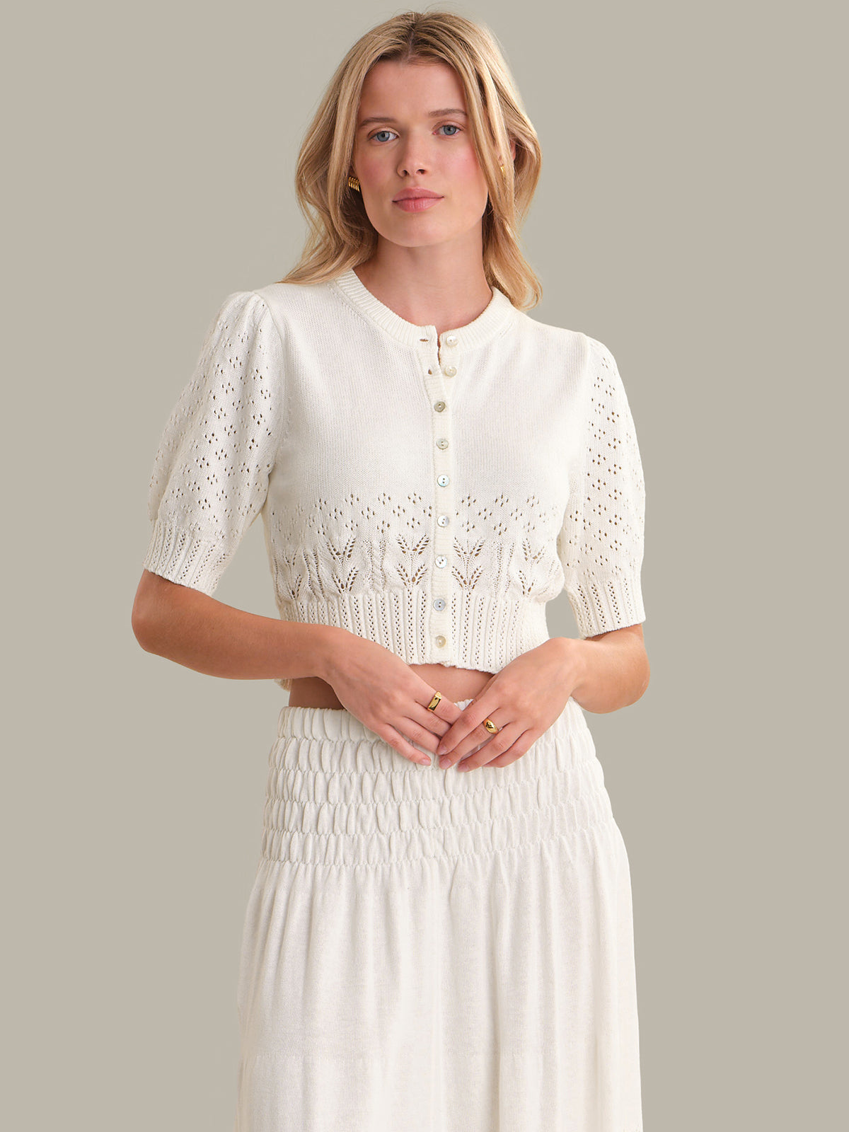 Woman wearing a white dress with lace details on a plain background