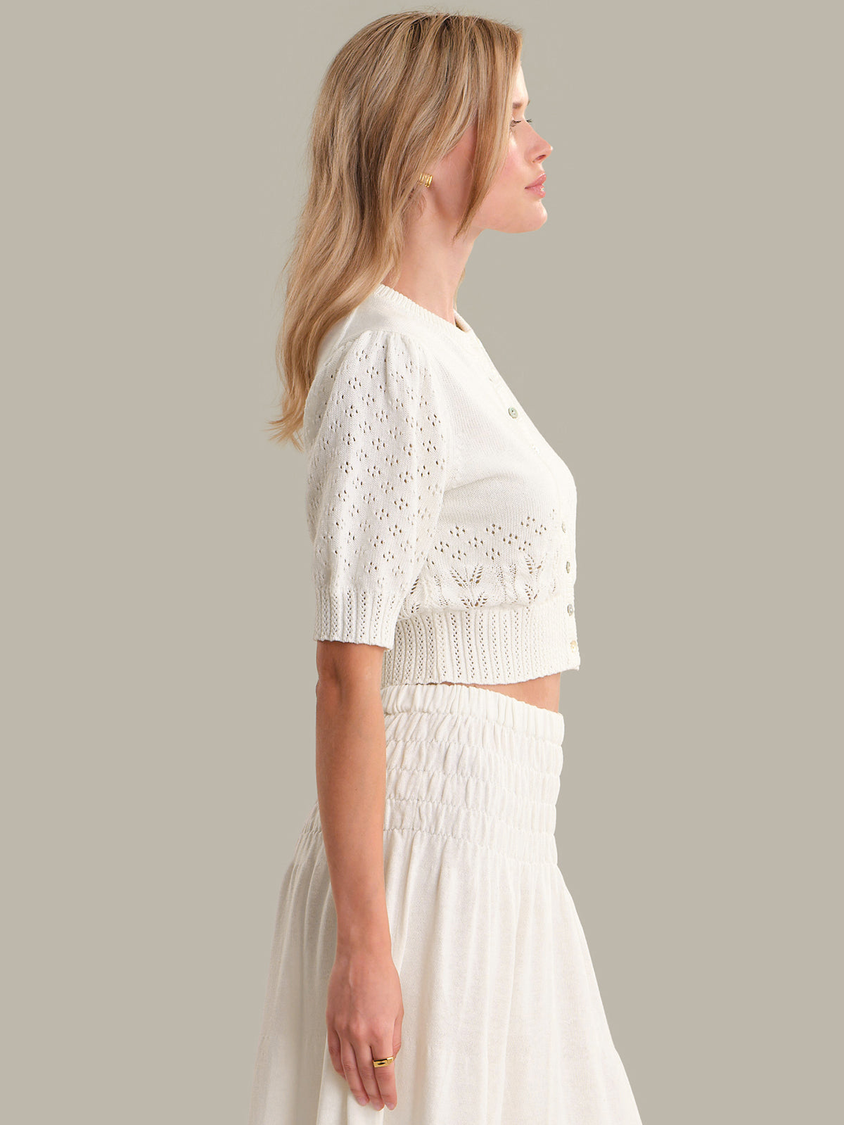 Woman wearing a white lace top and skirt against a plain background