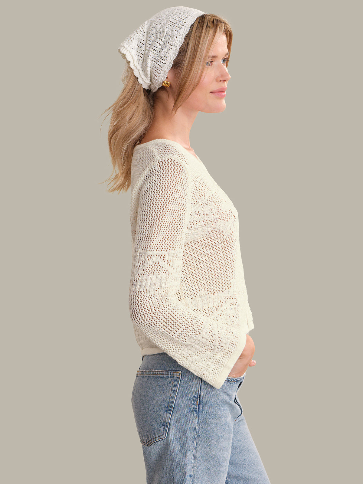 Woman wearing a white lace cardigan and light blue jeans on a plain background