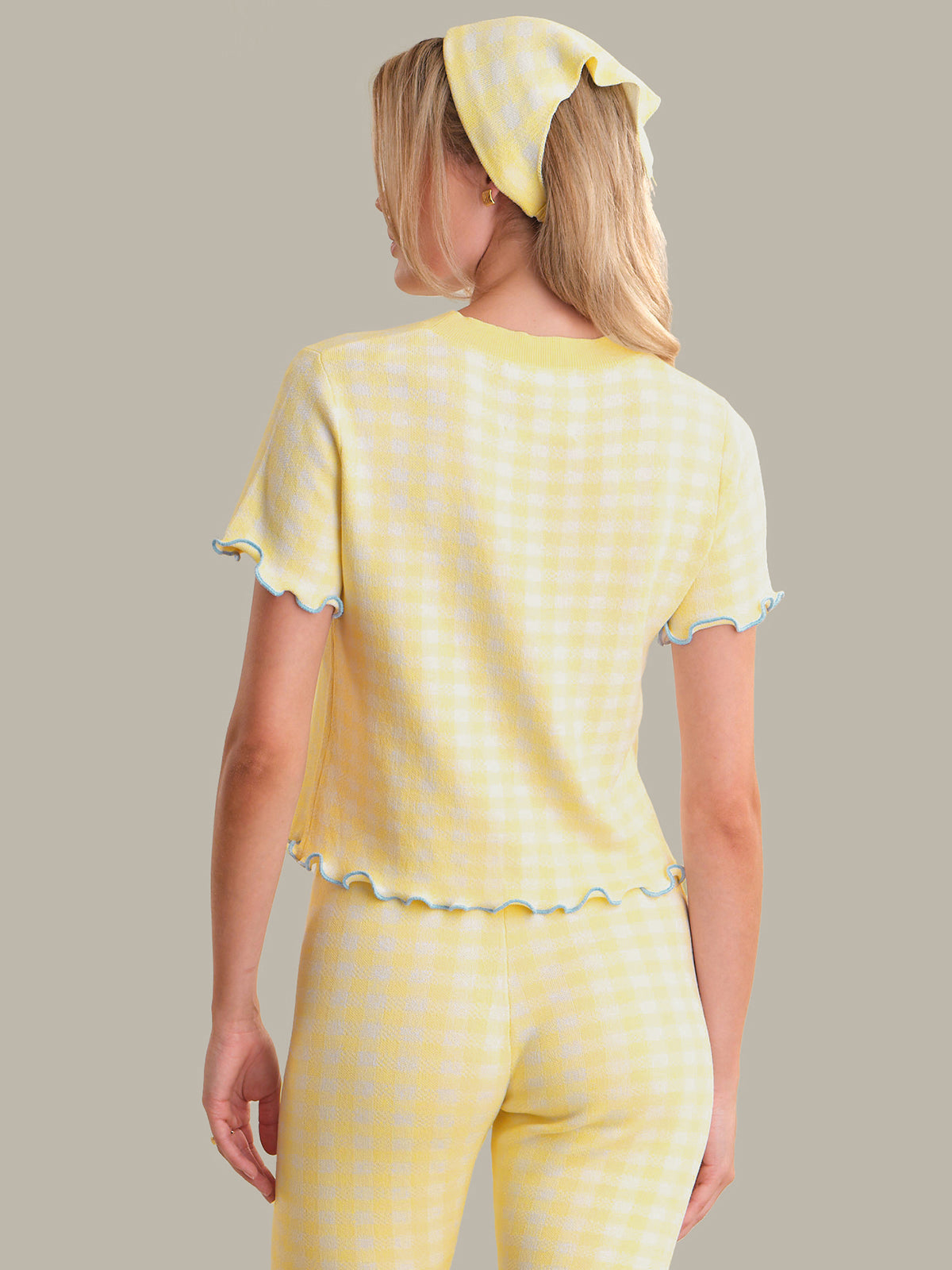 Woman wearing a yellow polka dot top with a matching headscarf on a plain background