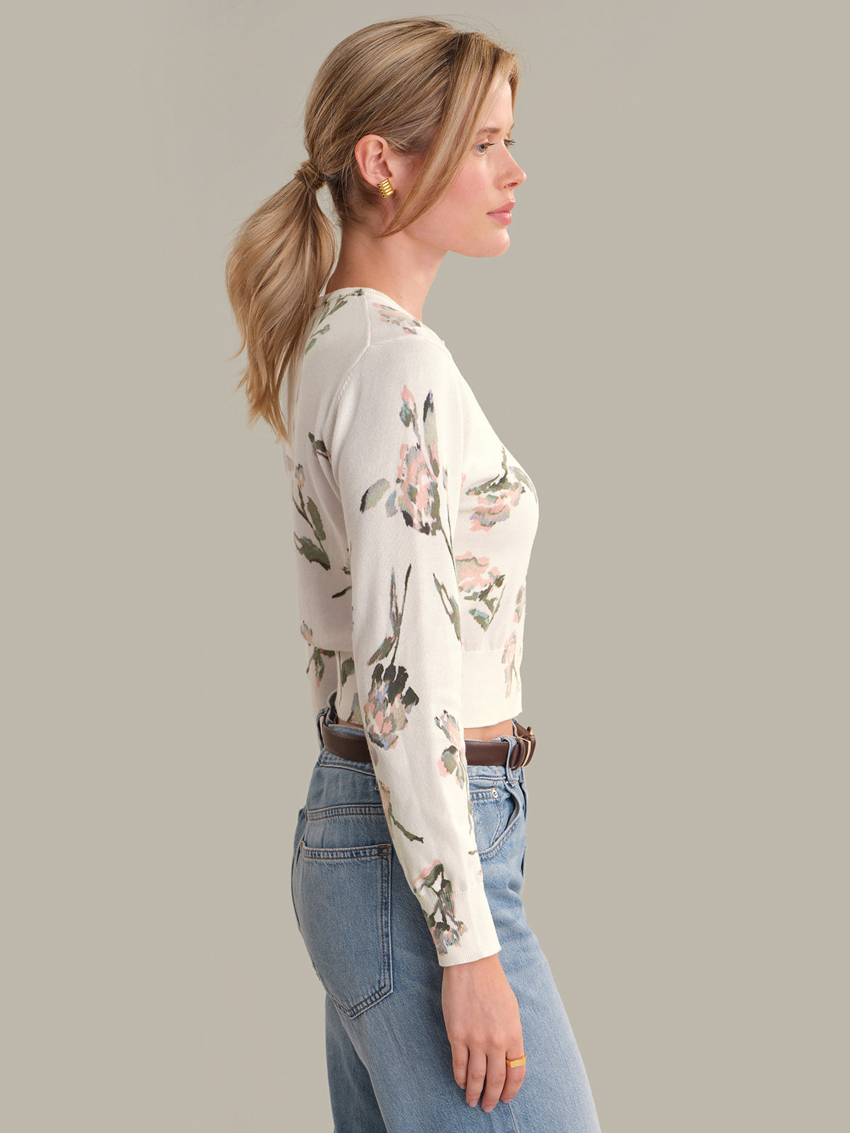 Woman wearing a floral long-sleeve cardigan and blue jeans on a gray background