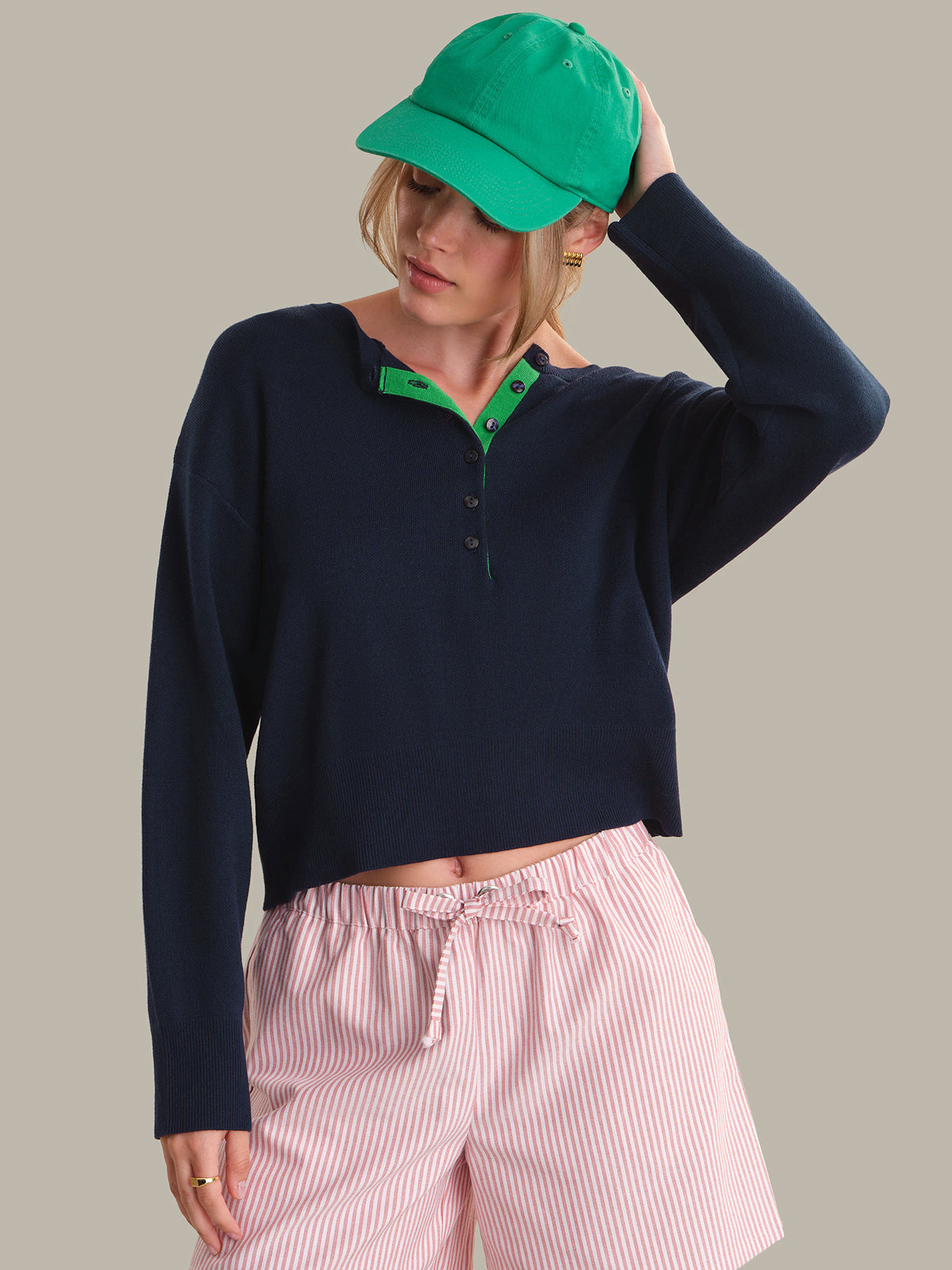 Person wearing a navy long-sleeve shirt with green trim and pink striped pants against a neutral background