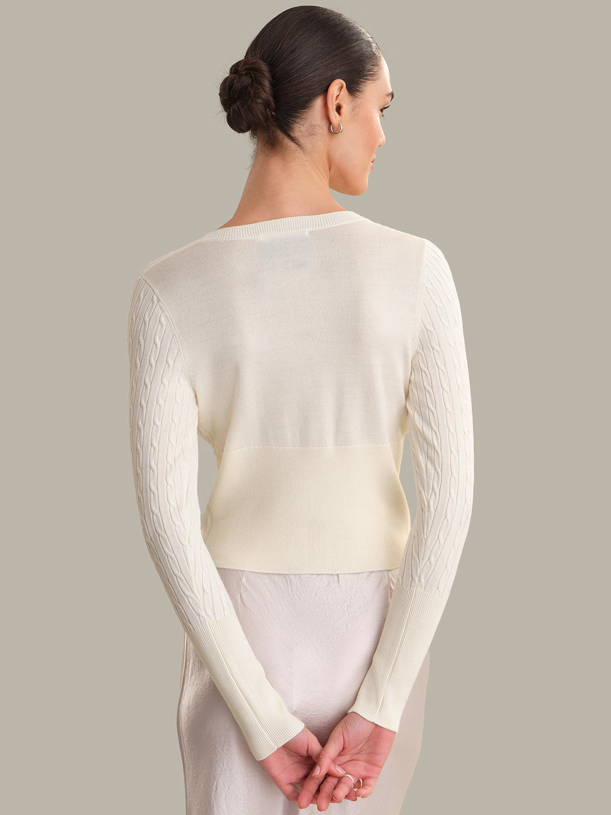 Woman wearing a light-colored long-sleeve top against a neutral background