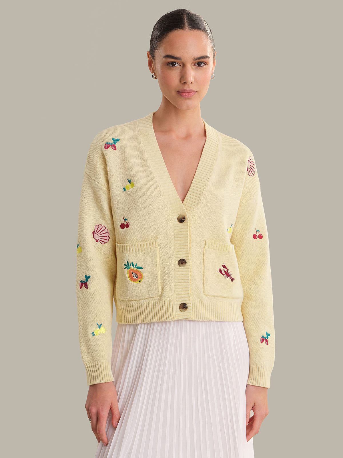 Woman wearing a light yellow cardigan with colorful embroidery on a neutral background