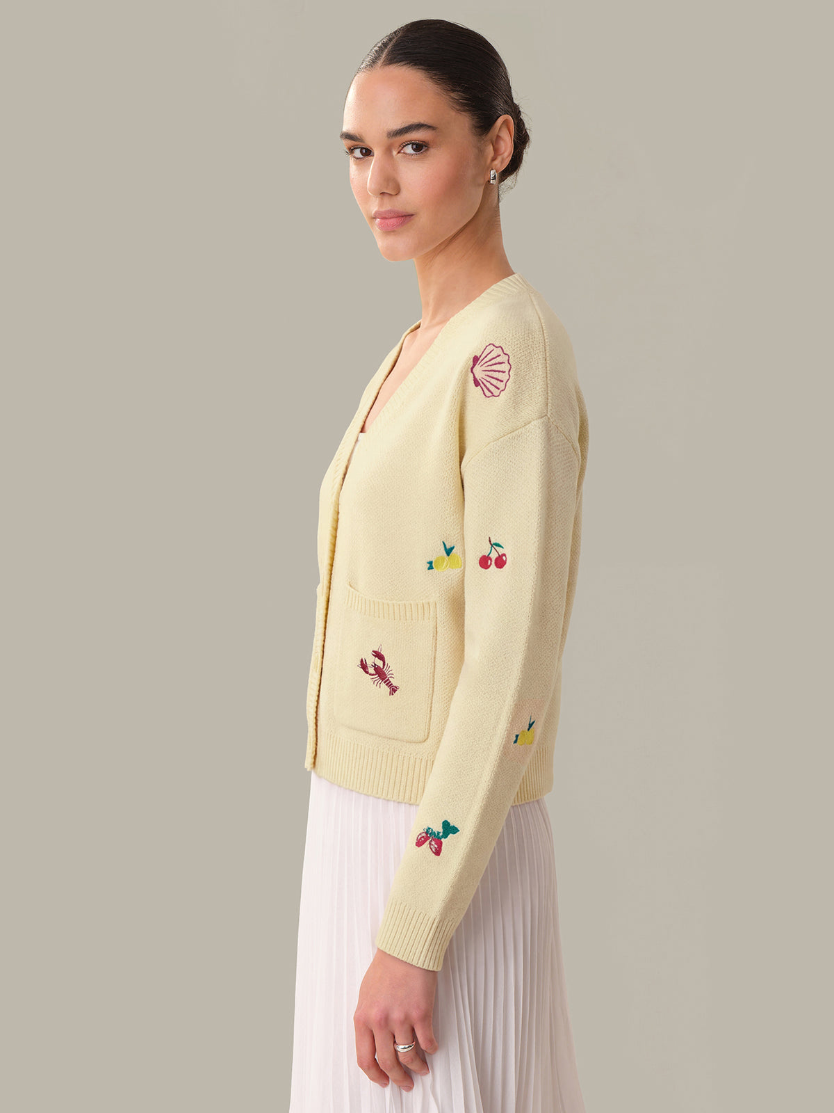 Woman wearing a light yellow cardigan with embroidered designs on a plain background