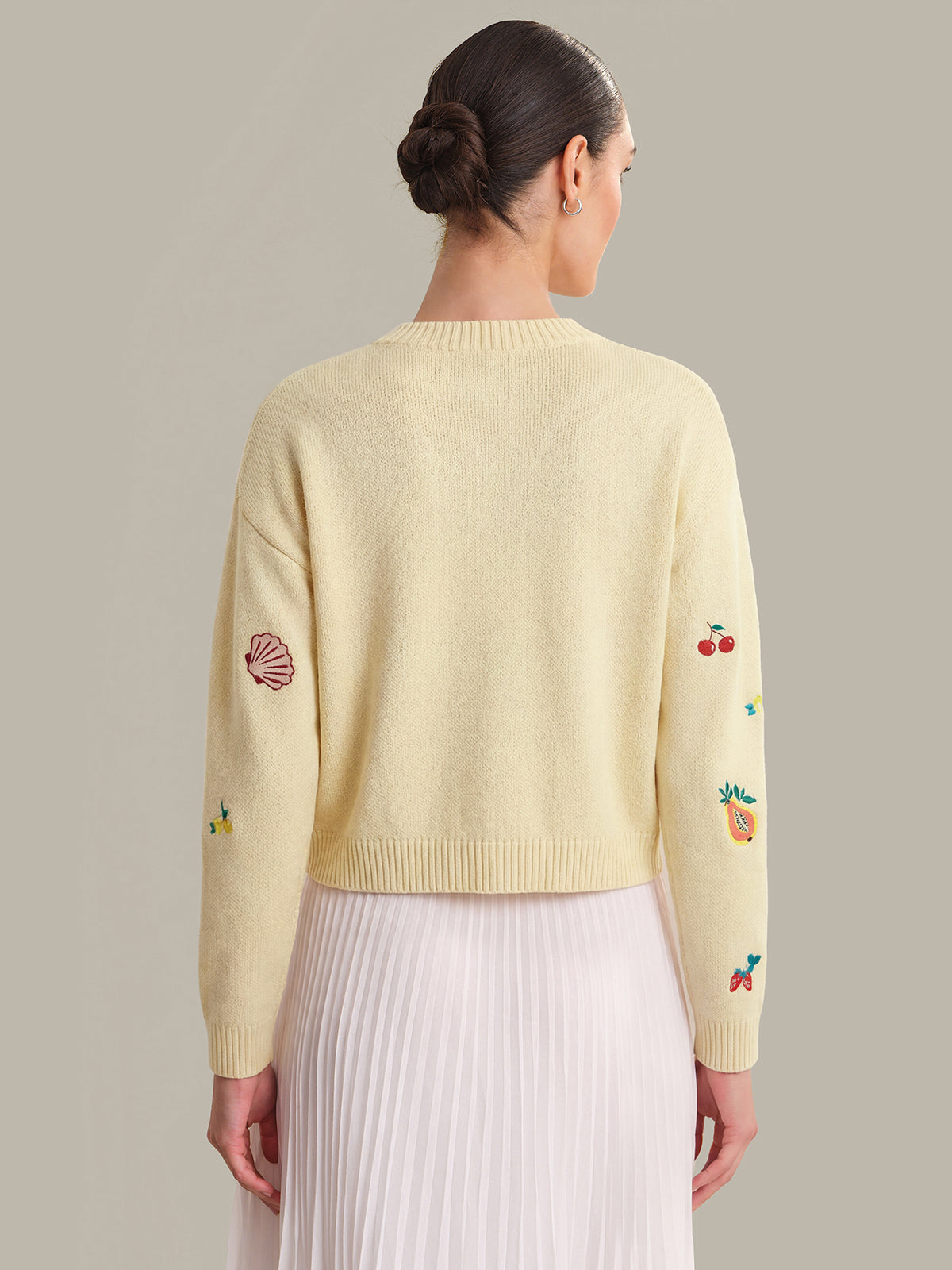 Woman wearing a light yellow sweater with embroidered designs on a plain background