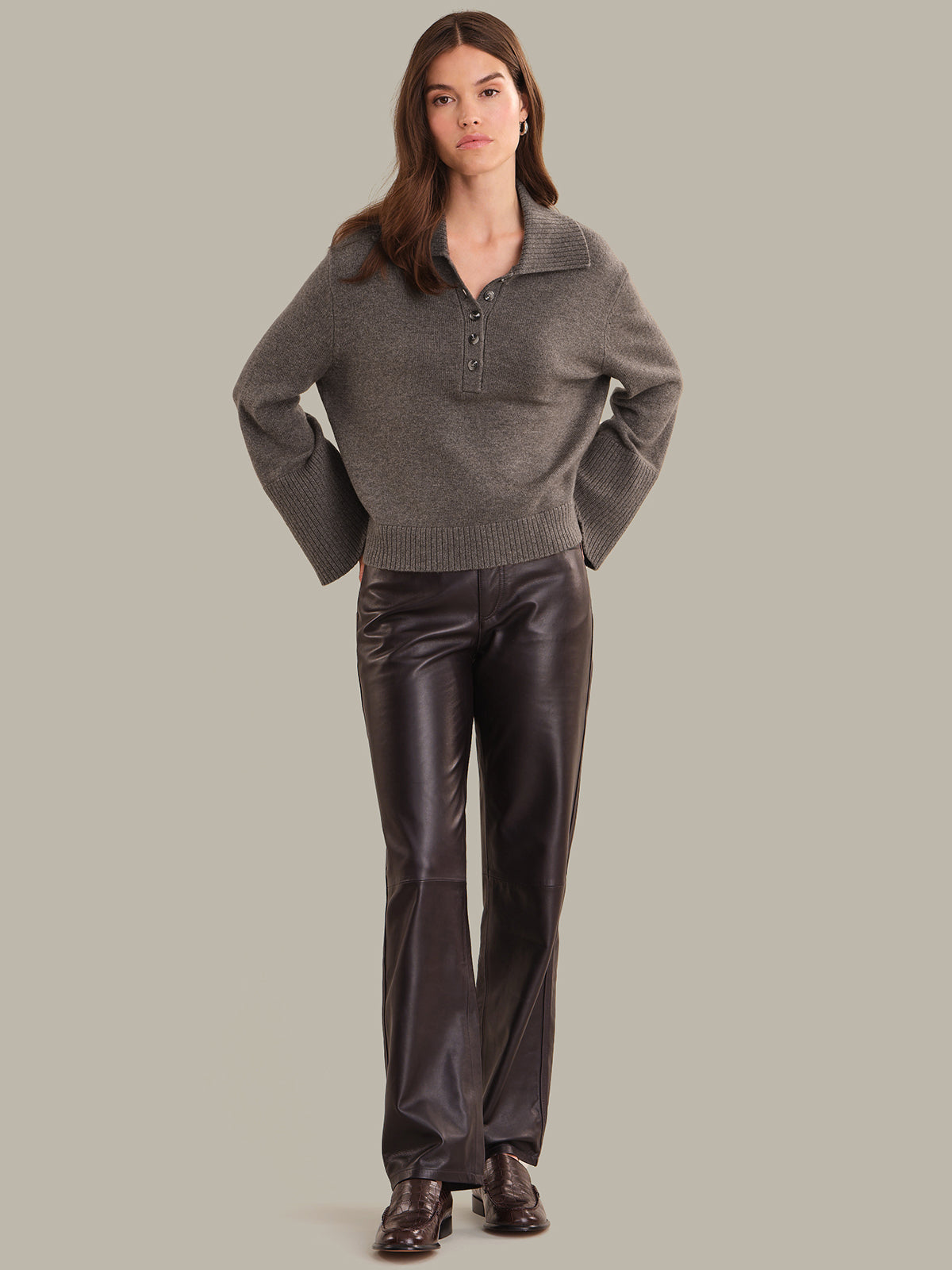 Woman wearing a gray sweater and dark pants against a plain background