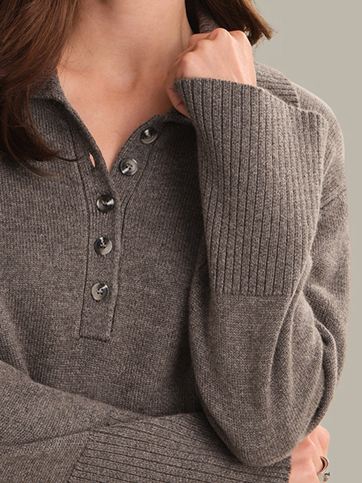 Close-up of a person wearing a gray ribbed sweater with button details.