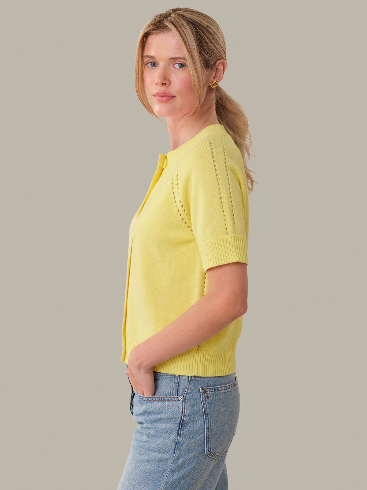 Woman wearing a yellow sweater and blue jeans against a plain background