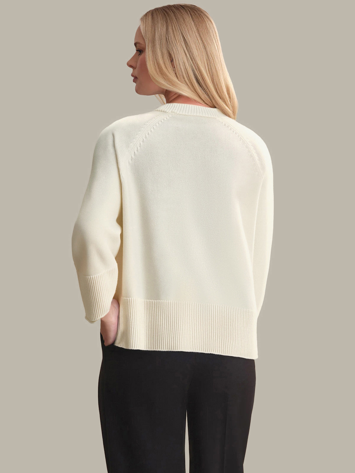 Woman wearing a cream sweater and black pants against a neutral background