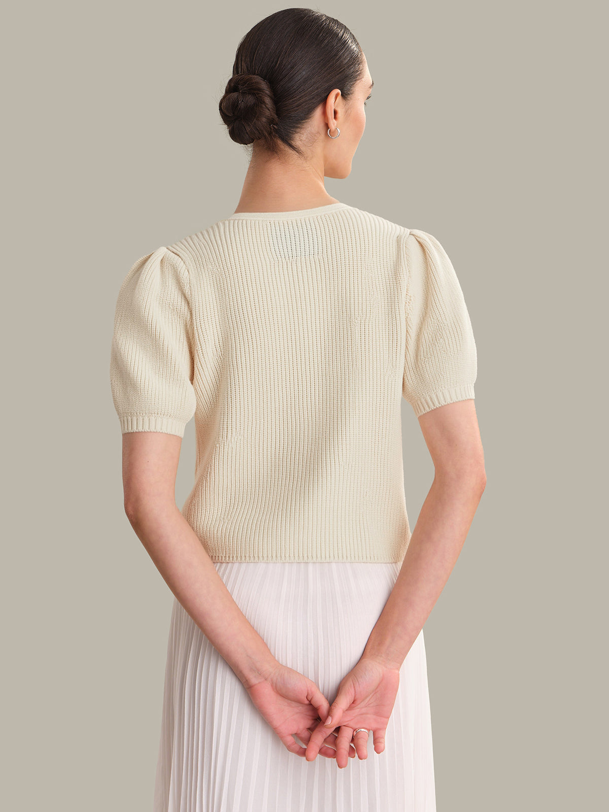 Woman wearing a light yellow ribbed sweater with short sleeves against a neutral background
