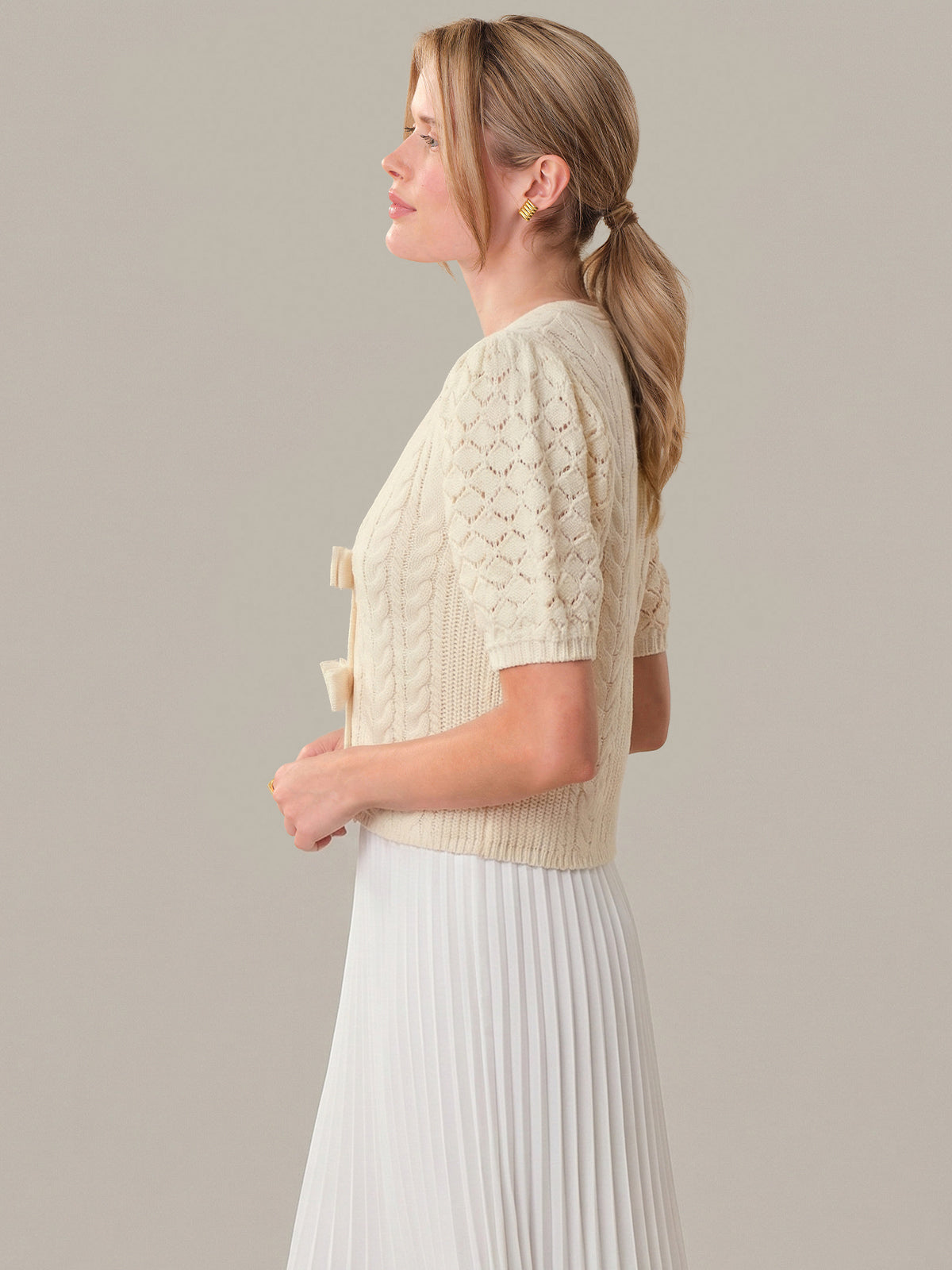 Woman wearing a beige knitted cardigan over a white dress on a plain background