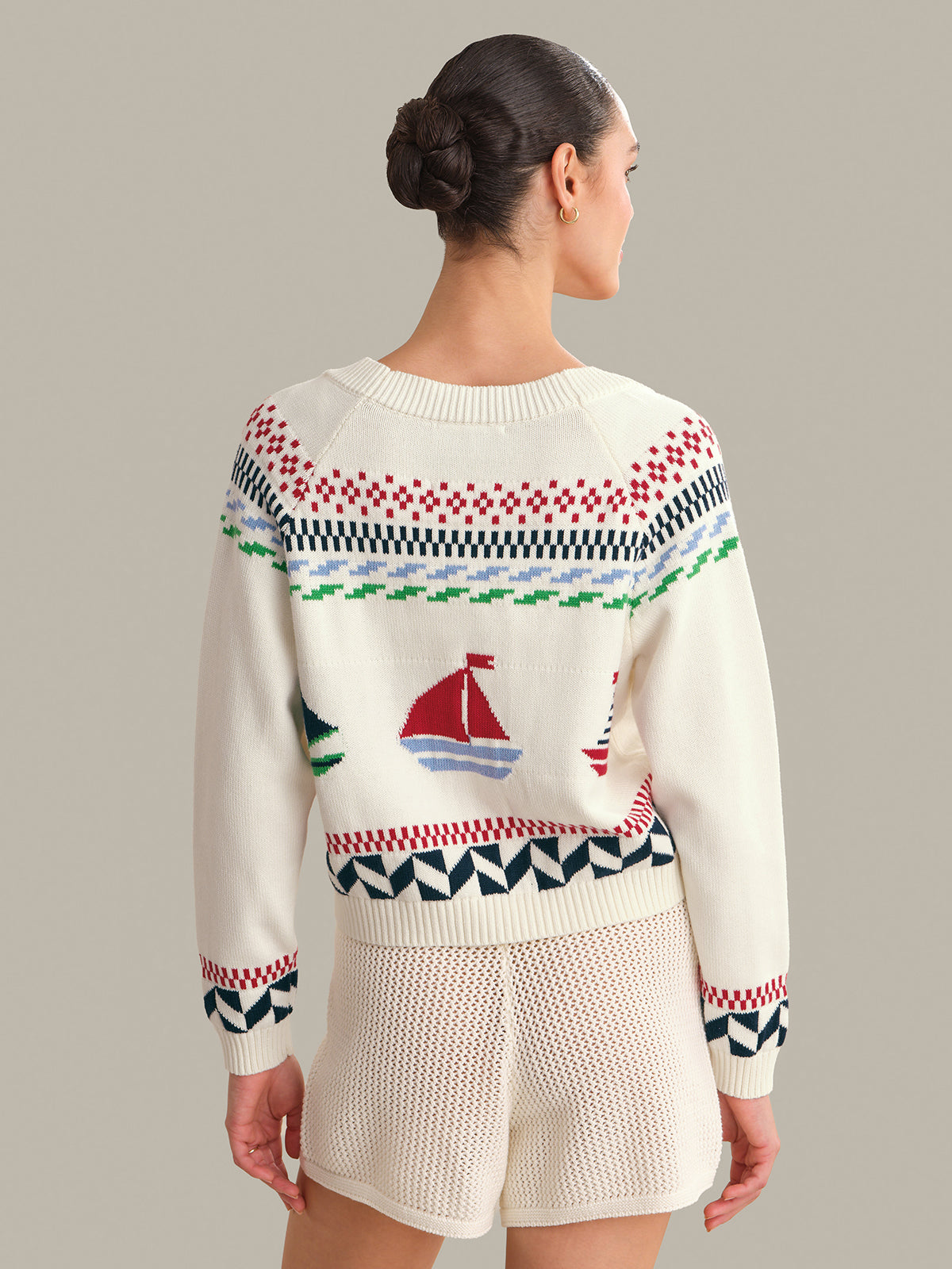 Woman wearing a patterned sweater with a sailboat design on a plain background