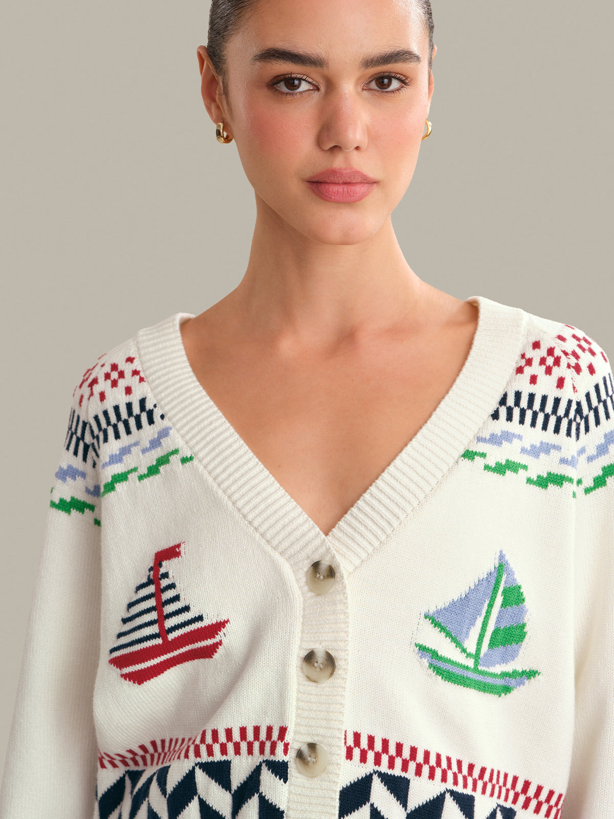 Woman wearing a white cardigan with colorful sailboat patterns on a neutral background