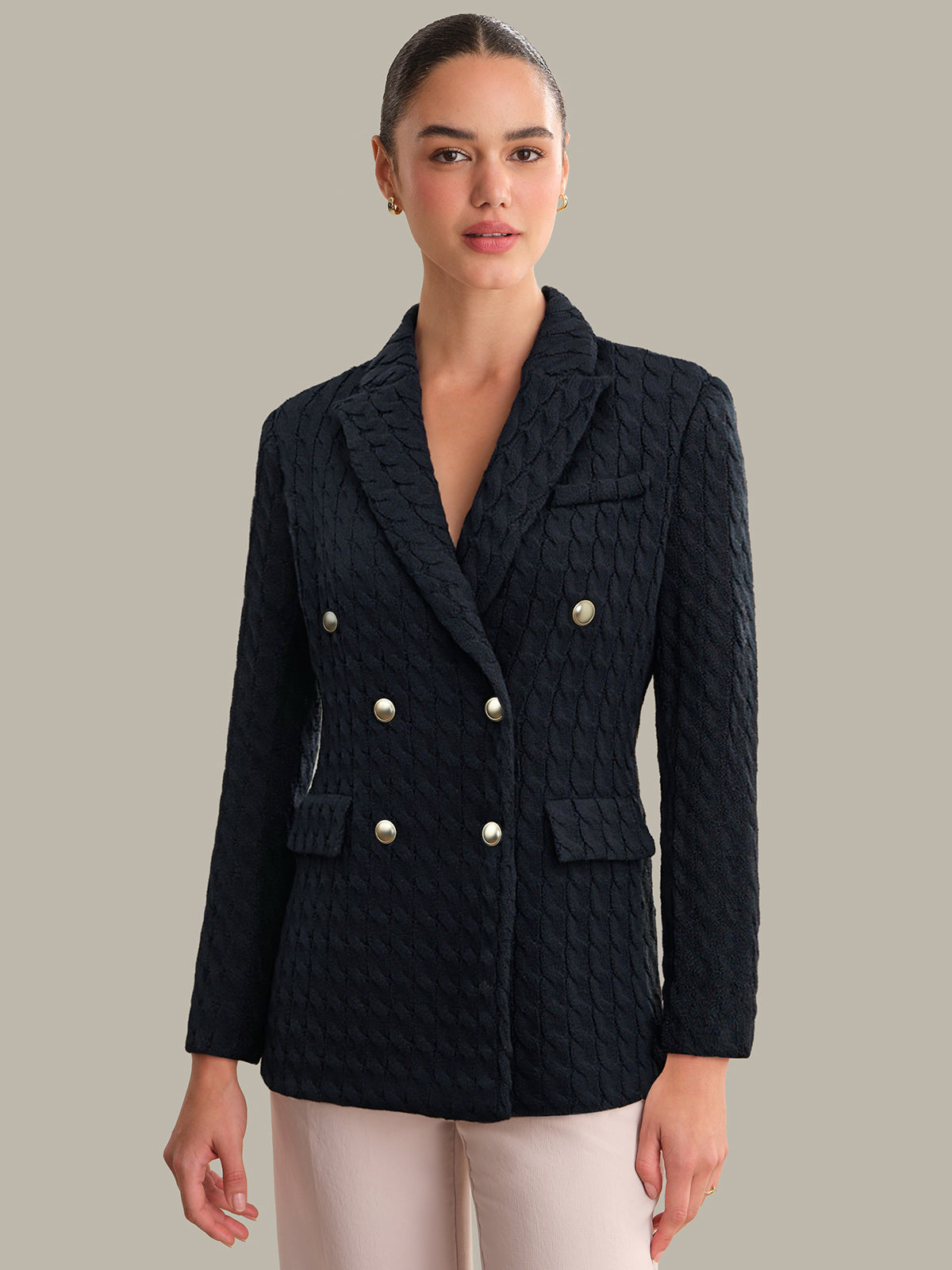 Woman wearing a dark quilted jacket with silver buttons on a neutral background