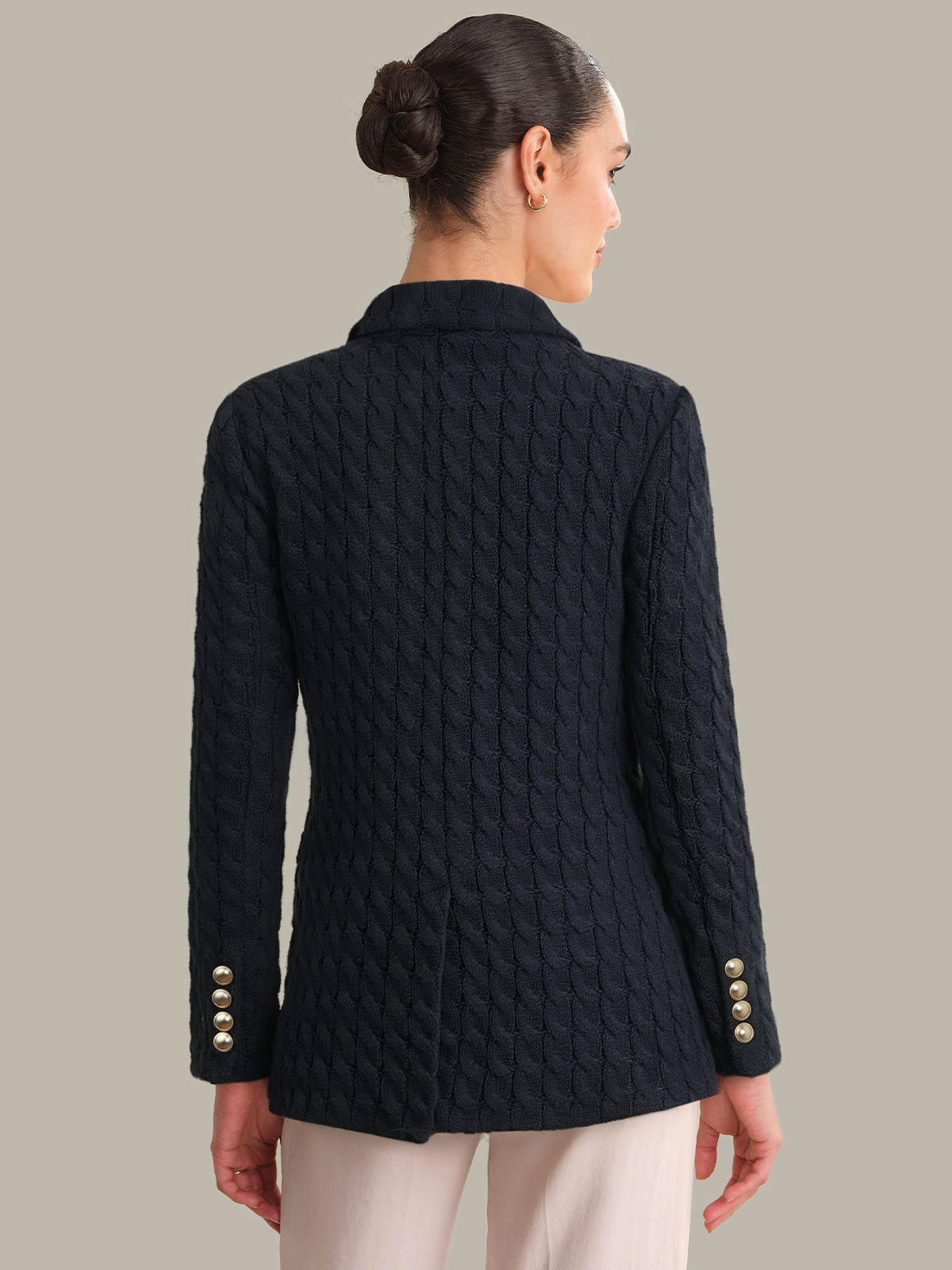 Woman wearing a black quilted jacket with gold buttons on a beige background